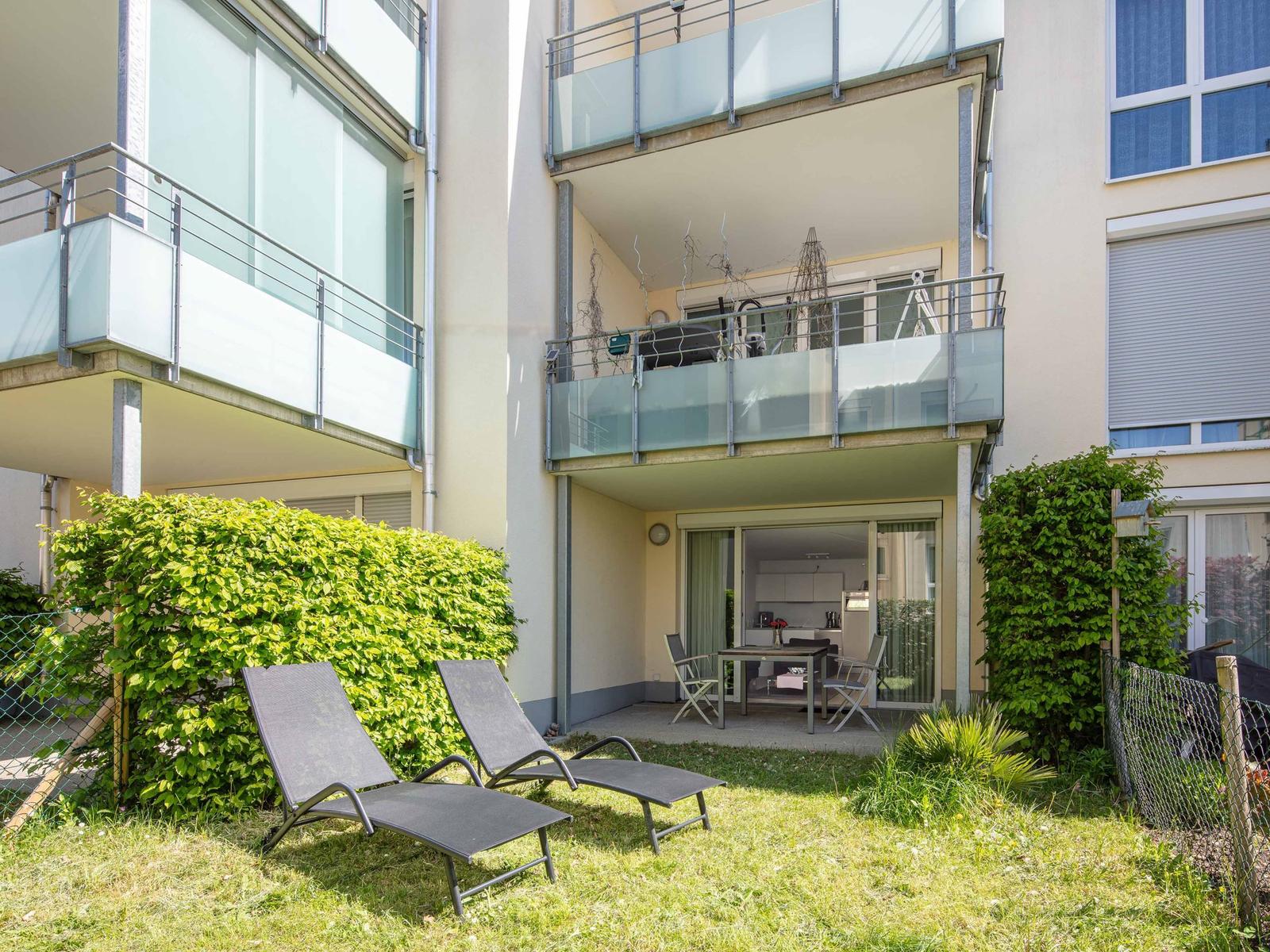 Hinterhof mit Liegestühlen und Balkon. Küche und Essbereich sind sichtbar.