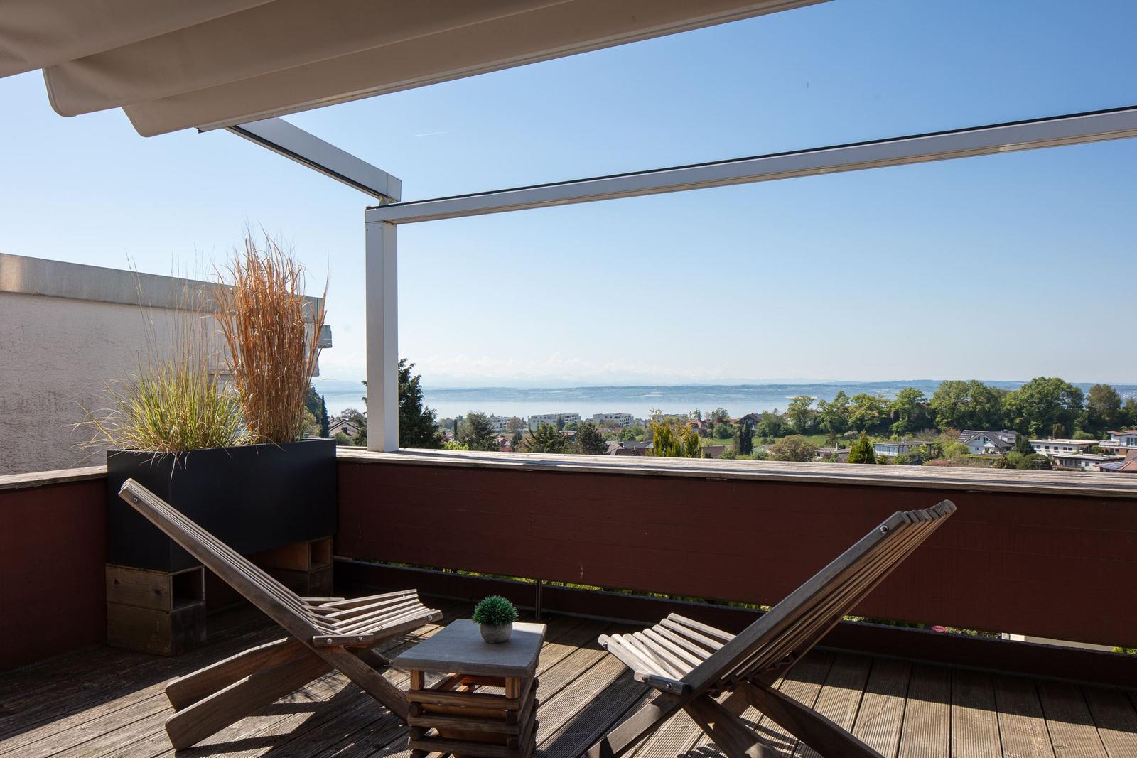 Terrasse mit Liegestühlen und Blick auf See und Landschaft.
