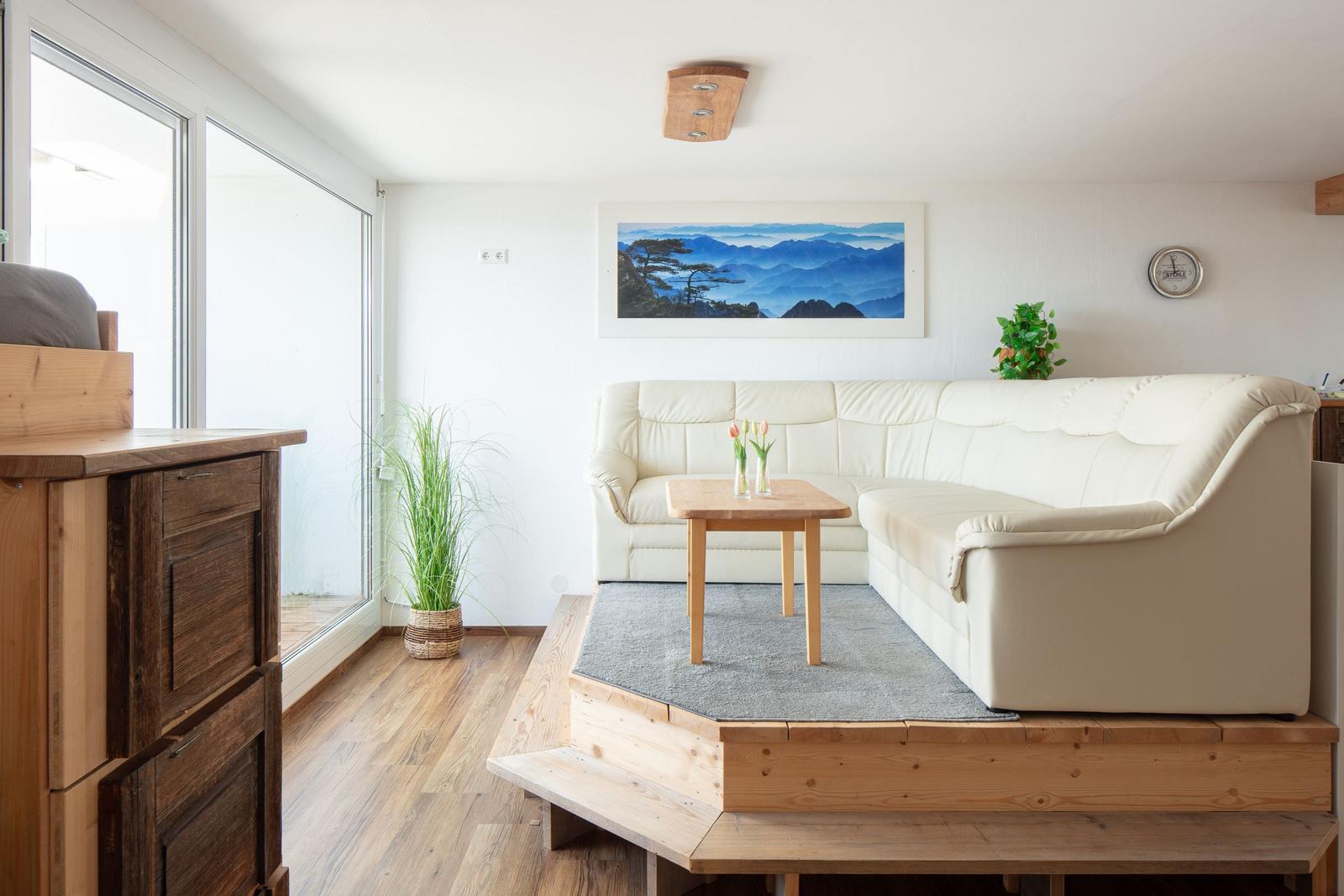Wohnzimmer mit weißem Sofa, Holztisch und Blick auf Balkon.