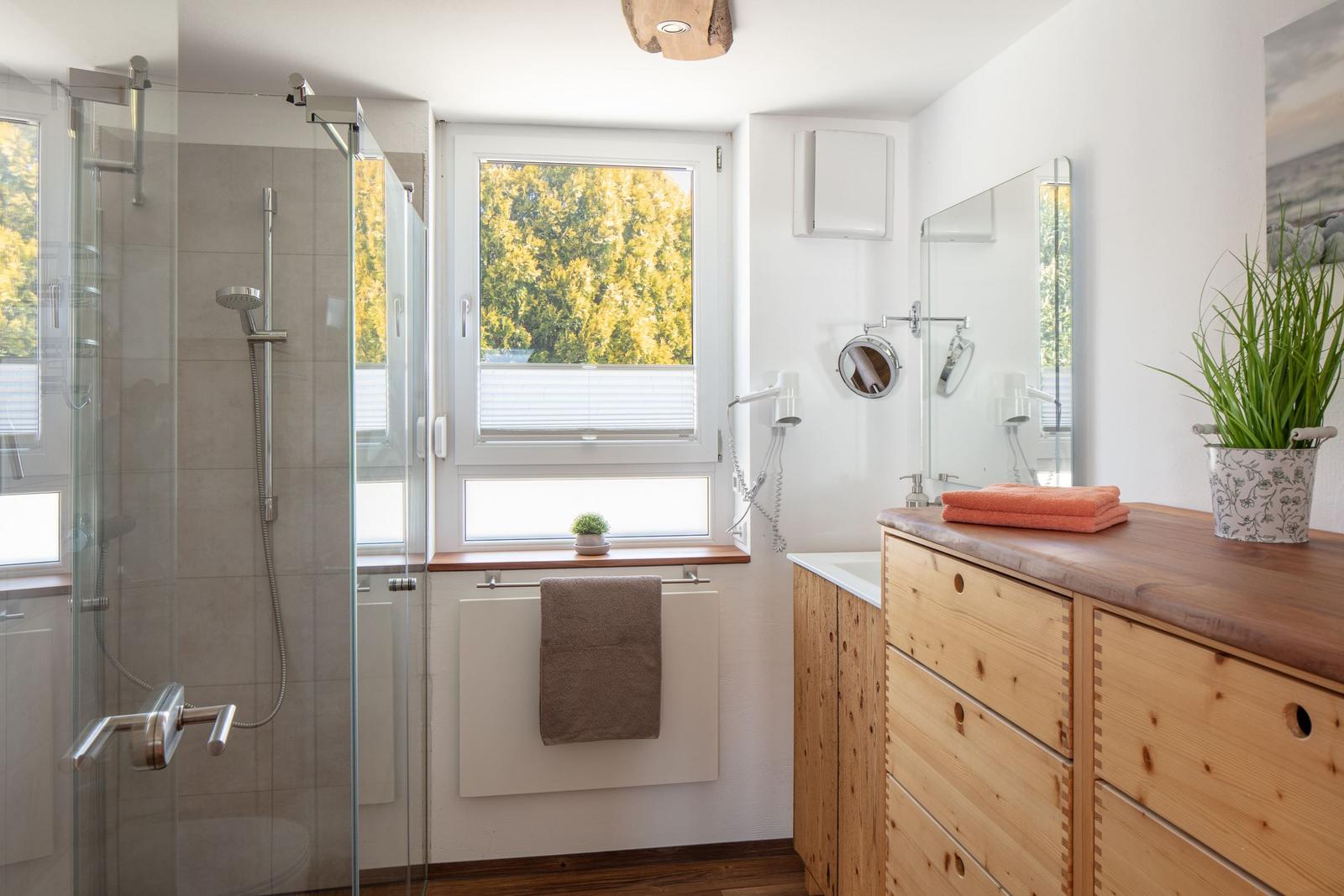 Badezimmer mit Dusche, Waschbecken und Fenster mit Blick auf Bäume.