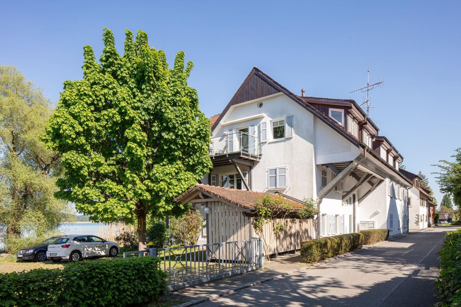 Ein zweistöckiges Haus mit Balkon, umgeben von Bäumen und einem Zaun.