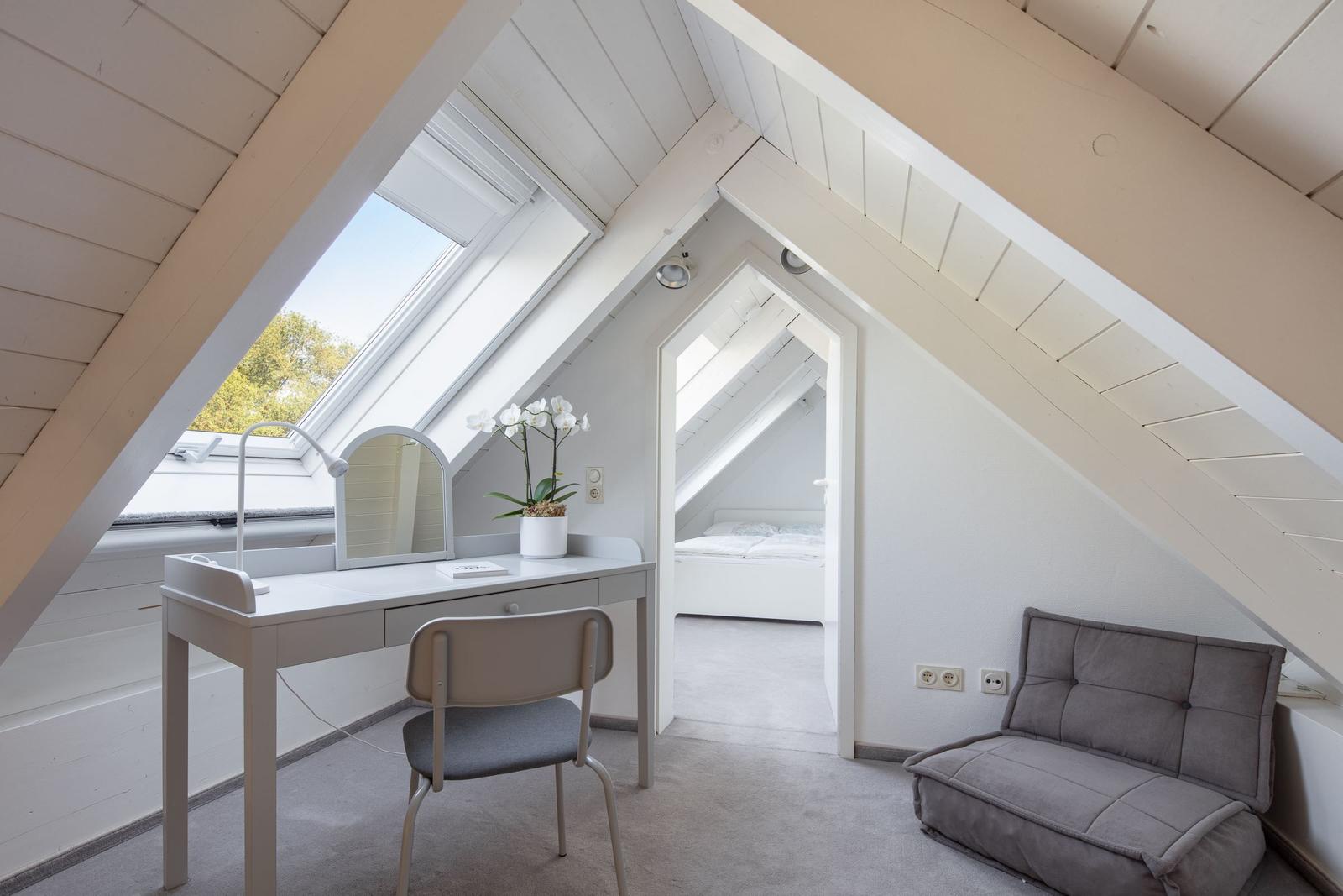 Schlafzimmer mit Dachbodenfenster, Schreibtisch und Sofa. Blick in Schlafbereich.