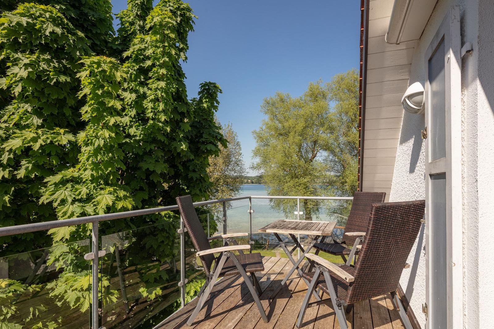 Terrasse mit Tisch und Stühlen, Blick auf Wasser und Bäume.
