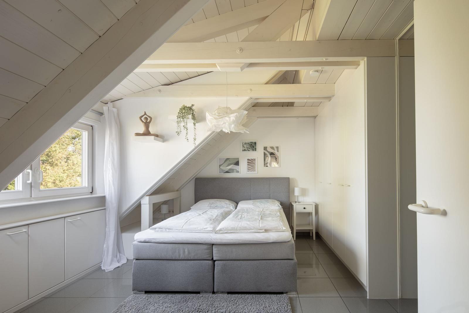 Schlafzimmer mit Dachschräge, Bett, Fenster und Schränken.