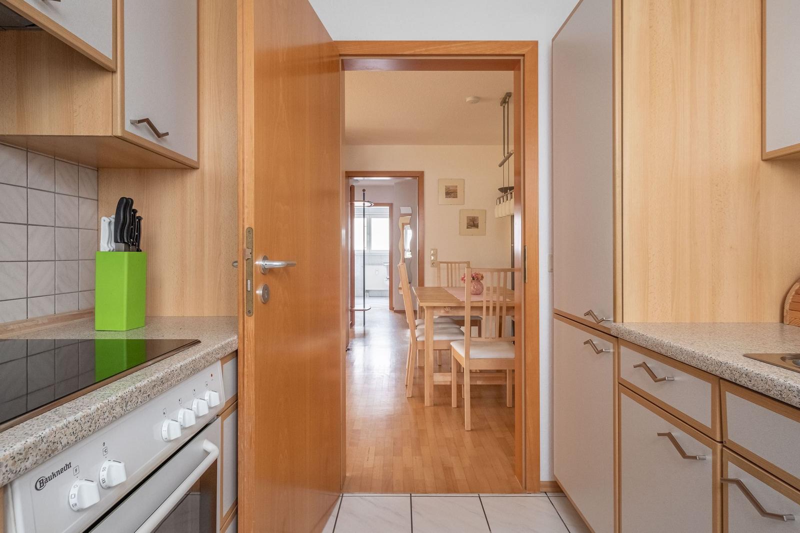 Küche mit Holzmöbeln und Blick in Esszimmer mit Tisch und Stühlen.