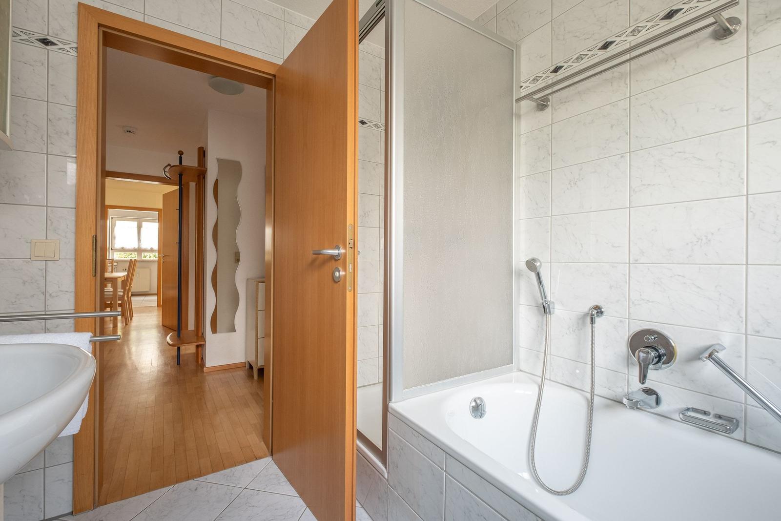 Badezimmer mit Badewanne und Dusche. Durchgang zur Küche und Schlafzimmer.