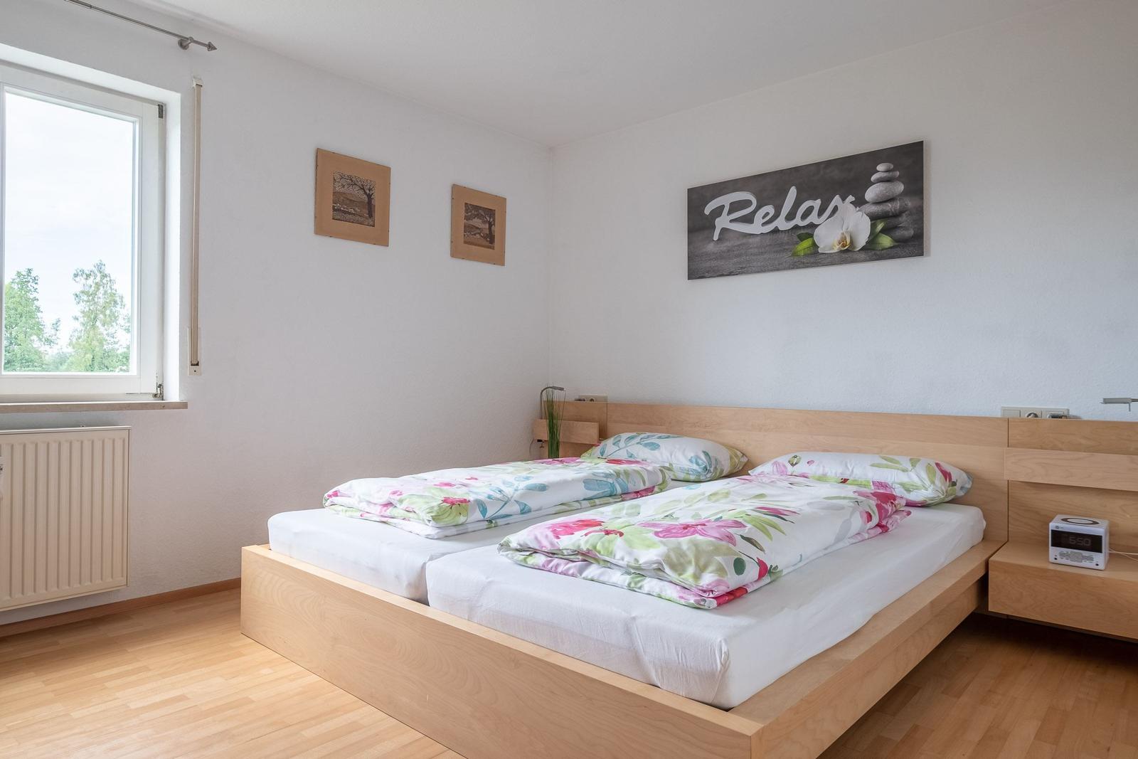 Schlafzimmer mit Doppelbett, Fenster und Wandbild mit Relax.