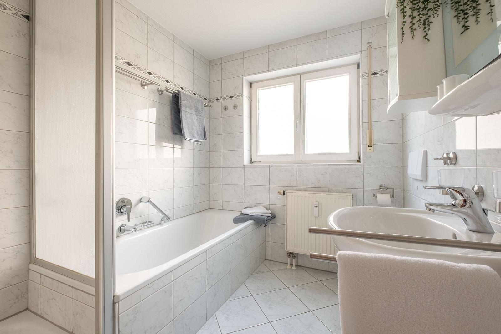Bad mit Badewanne, Waschbecken und Fenster. Fliesenwand und -boden.