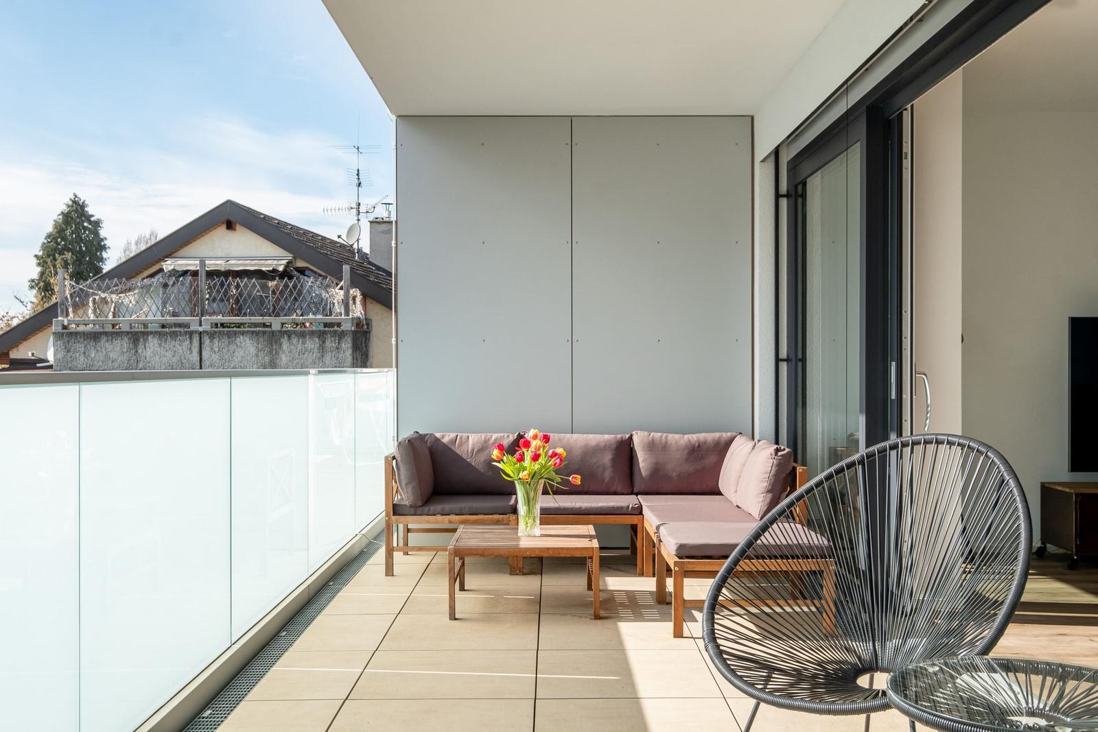 Terrasse mit Sitzgruppe, Tisch und Stuhl. Glasgeländer und Blick auf Nachbarhaus.