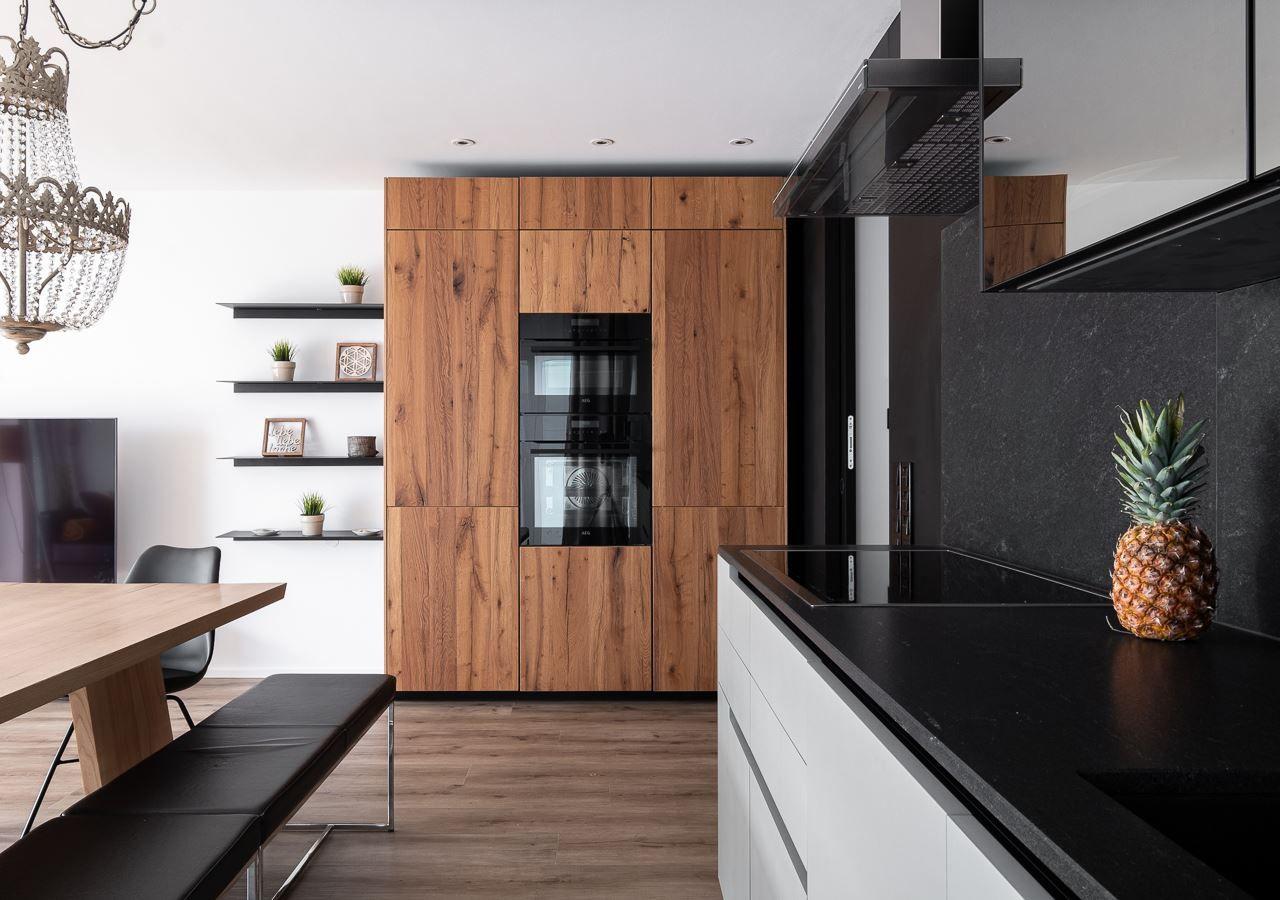 Moderne Küche mit Holzschränken, schwarzer Arbeitsplatte und integriertem Backofen.