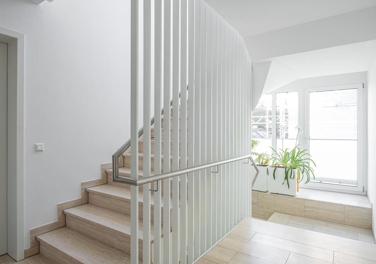 Treppenhaus mit Holztreppe, weißem Geländer und Pflanzen an Fenster