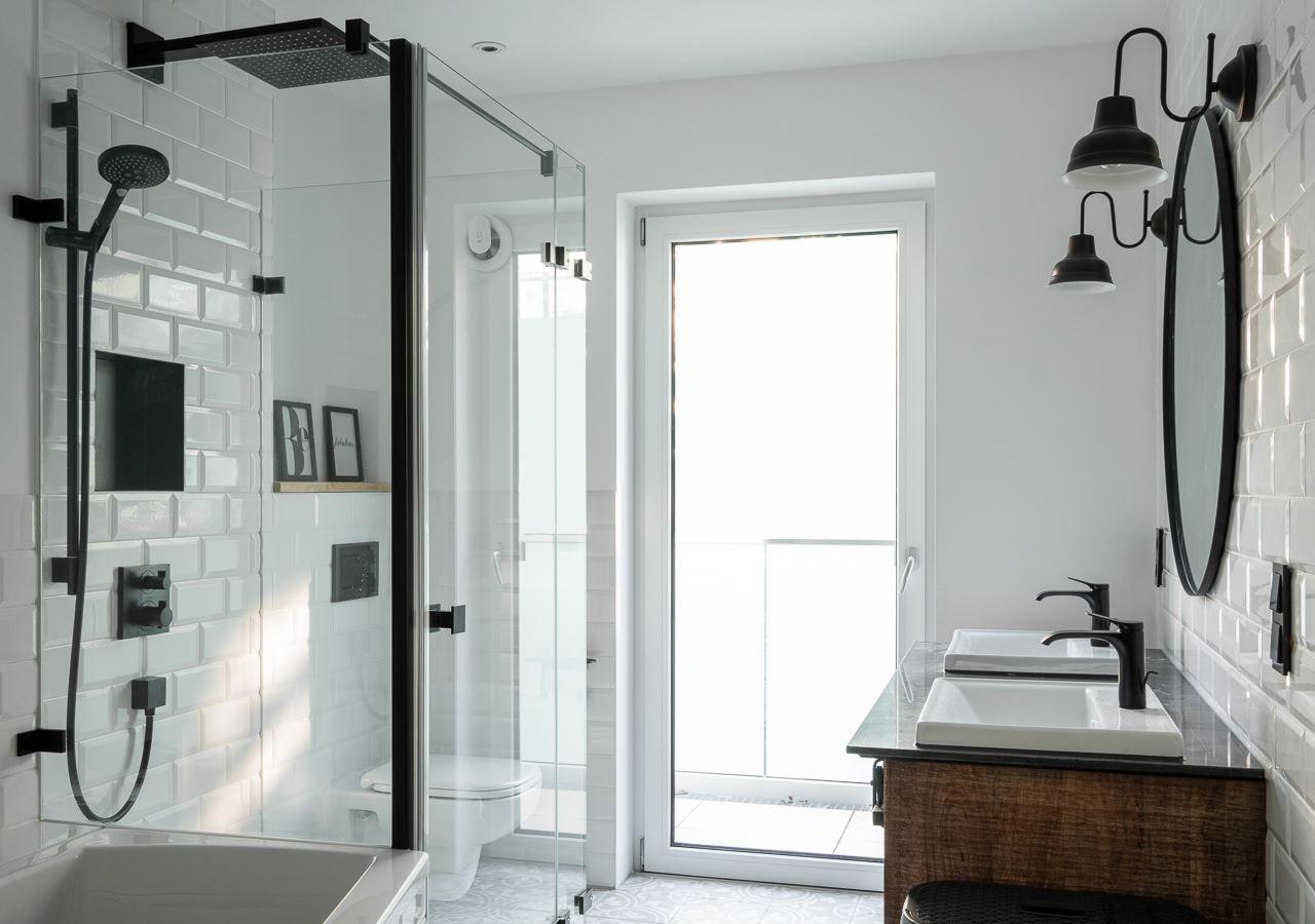 Badezimmer mit Dusche, Waschbecken und Toilette. Weiße Fliesen und schwarze Armaturen.
