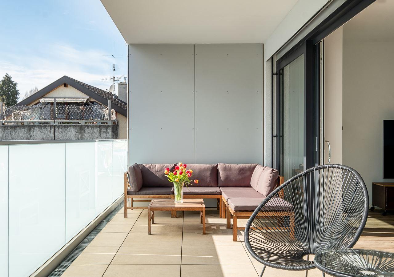Terrasse mit Sitzgruppe, Tisch und Stuhl. Glasgeländer und Blick auf Nachbarhaus.