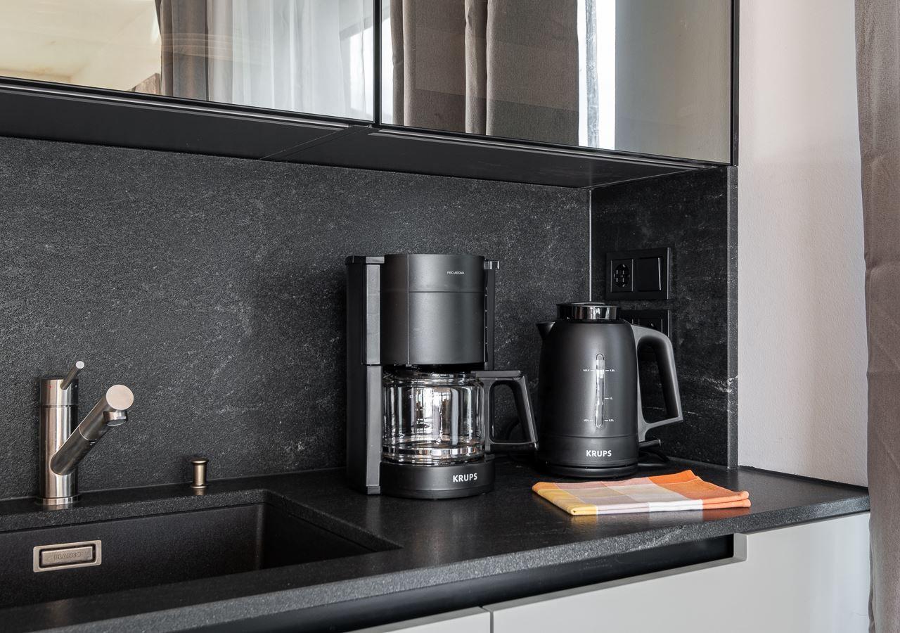 Küchenbereich mit Kaffeemaschine und Wasserkocher auf dunkler Arbeitsplatte.