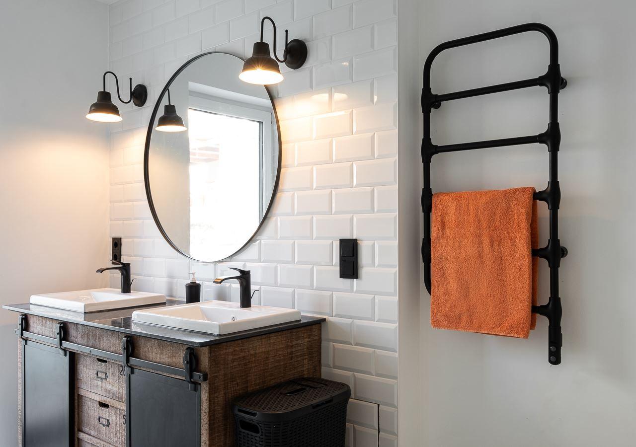 Badezimmer mit zwei Waschbecken, runden Spiegel und Handtuchwärmer mit orangefarbenem Handtuch.