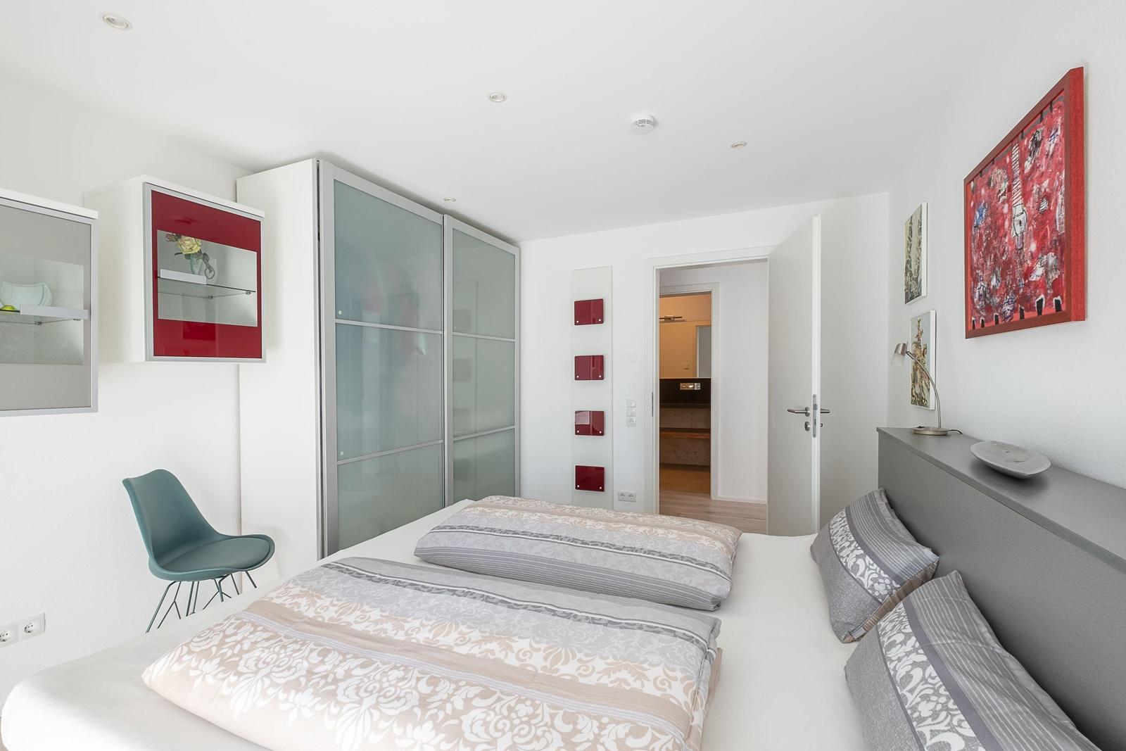 Schlafzimmer mit Doppelbett, Glaswand-Schrank und rotem Kunstwerk an der Wand.