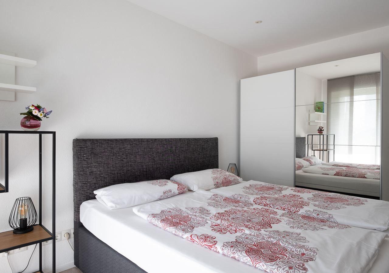 Schlafzimmer mit Doppelbett, Spiegelschrank und Nachttisch mit Lampe.