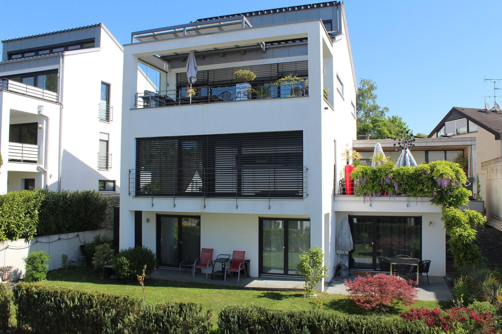 Modernes Haus mit Balkon, Terrasse und Garten. Schwarze Fensterläden und weiße Fassade.