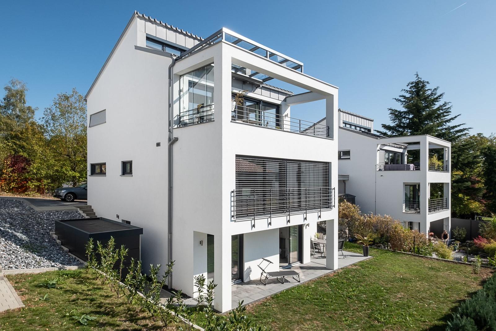 Moderne weiße Villa mit Balkon und Garten. Poolbereich und Terrasse sichtbar.