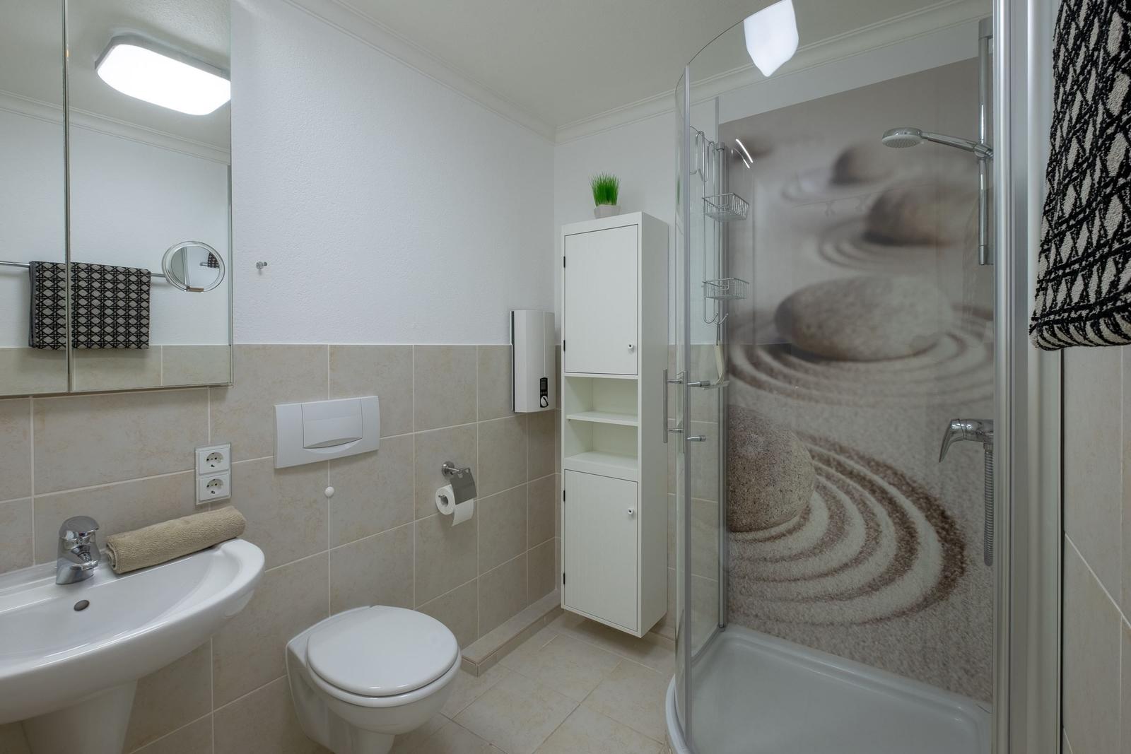 Badezimmer mit Dusche, Waschbecken und Toilette. Glaswand mit Steinmuster.