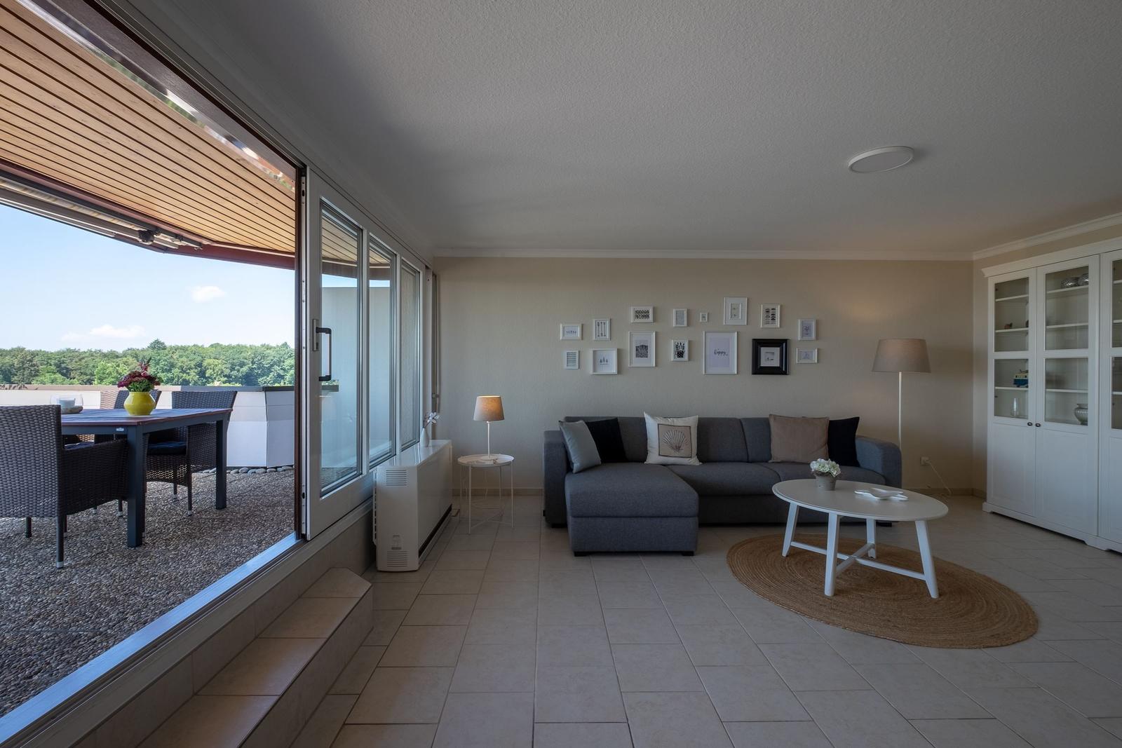 Wohnbereich mit Sofa, Couchtisch und Blick auf Terrasse mit Tisch und Stühlen.