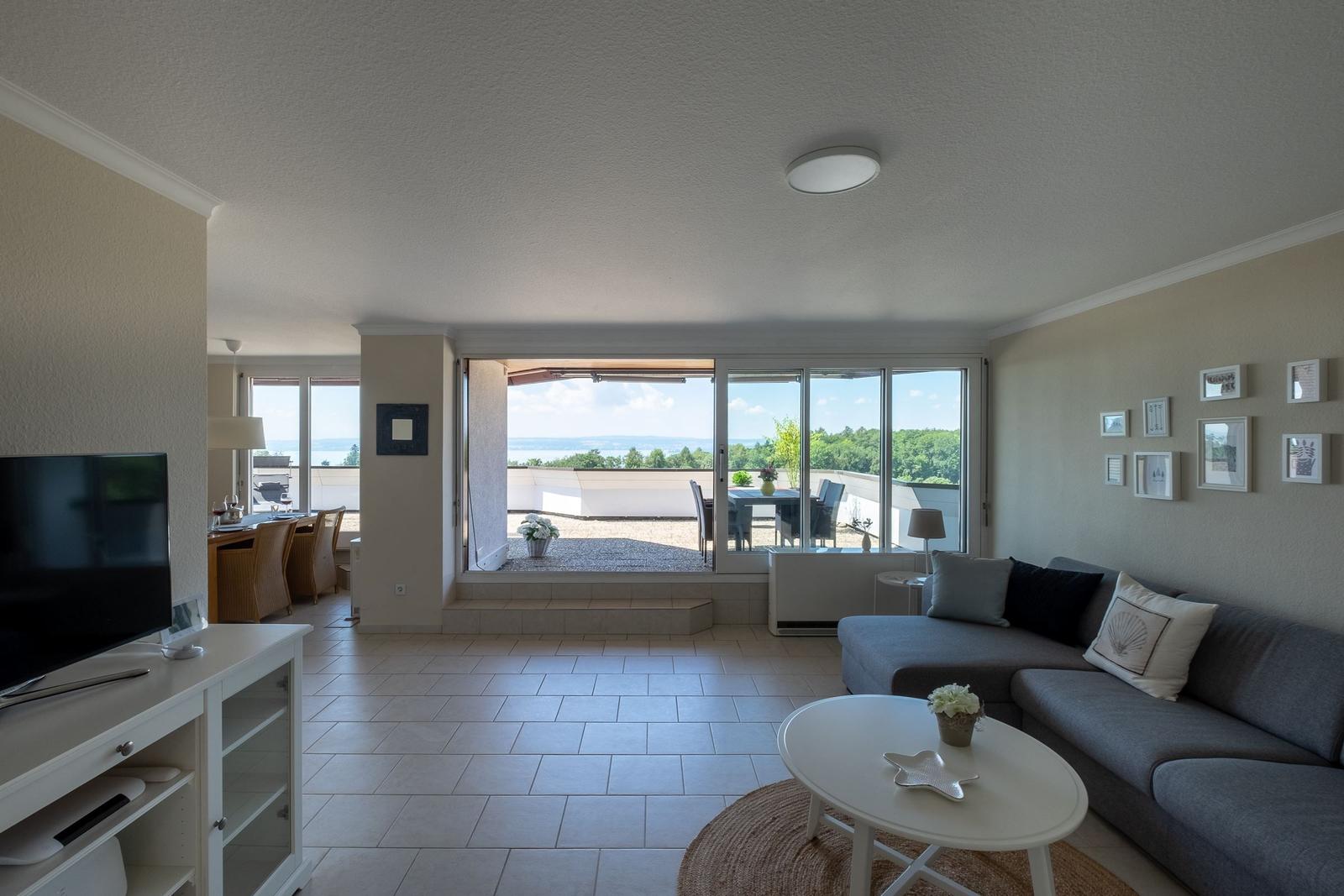 Wohnzimmer mit Sofa, TV und Blick auf Terrasse mit Gartenansicht.
