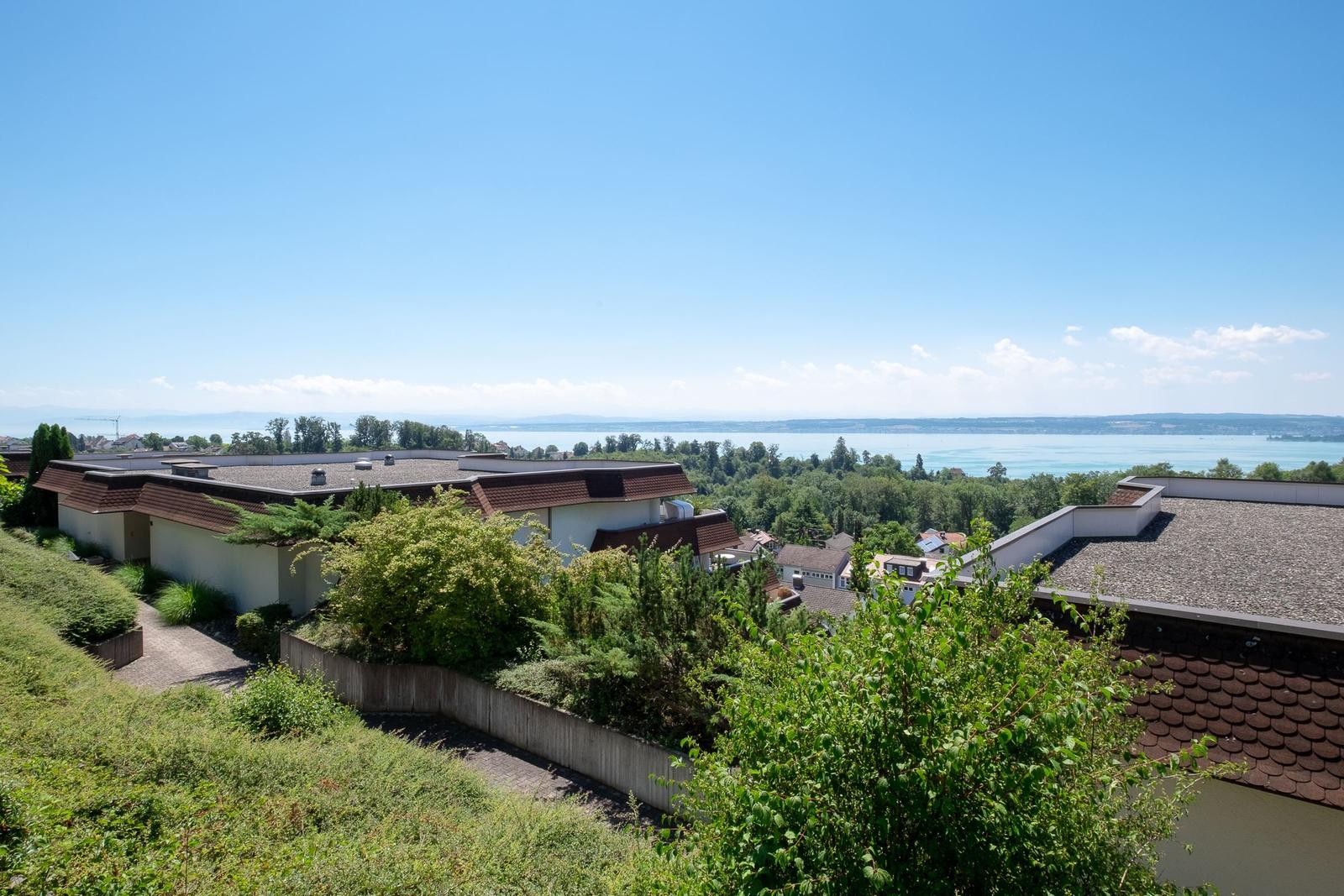 Haus mit Blick auf See und grüne Landschaft unter blauem Himmel.