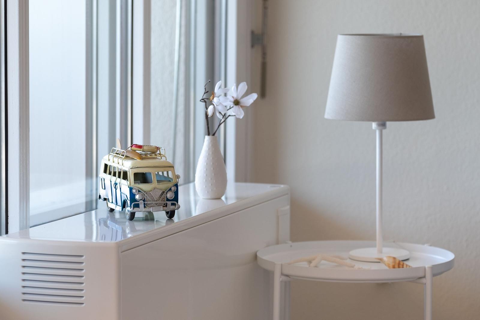 Auf dem Fensterbrett steht ein Modellbus mit Surfbrett, daneben ein Vasen mit Blumen und eine Lampe.