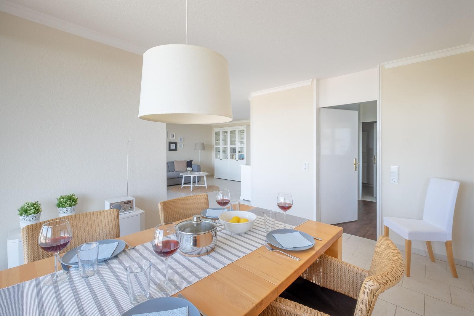 Esszimmer mit Tisch, Stühlen und Wein. Im Hintergrund Wohnzimmer mit Sofa und Glaswand.