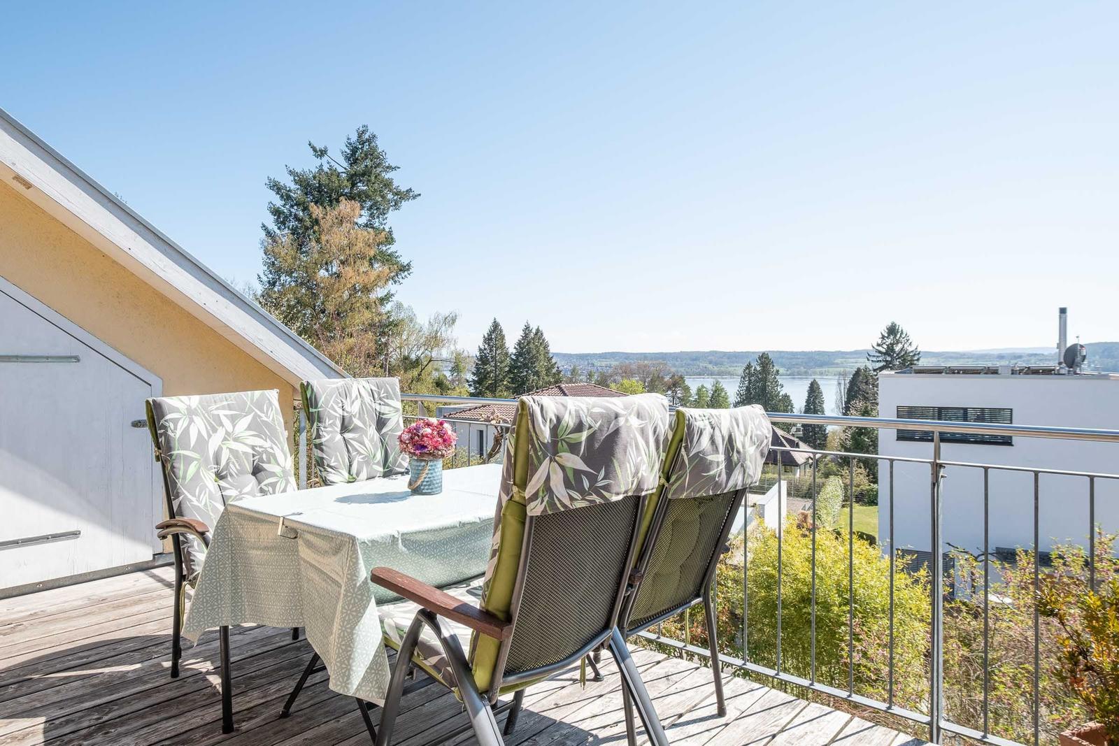 Terrasse mit Tisch und Stühlen, Blick auf See und Bäume.
