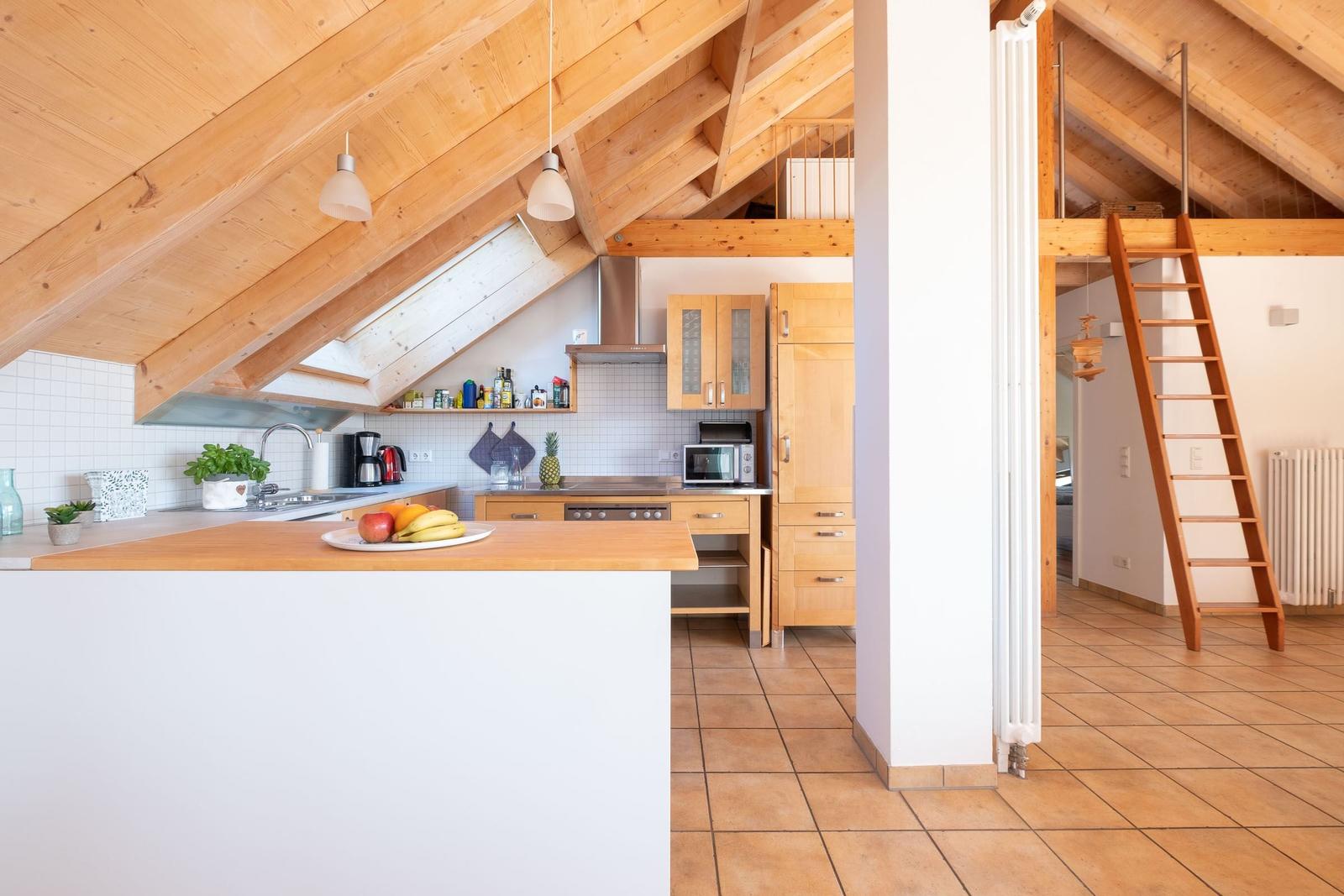 Küche mit Holzdecke und Treppe zur Galerie. Arbeitsplatte mit Obst.