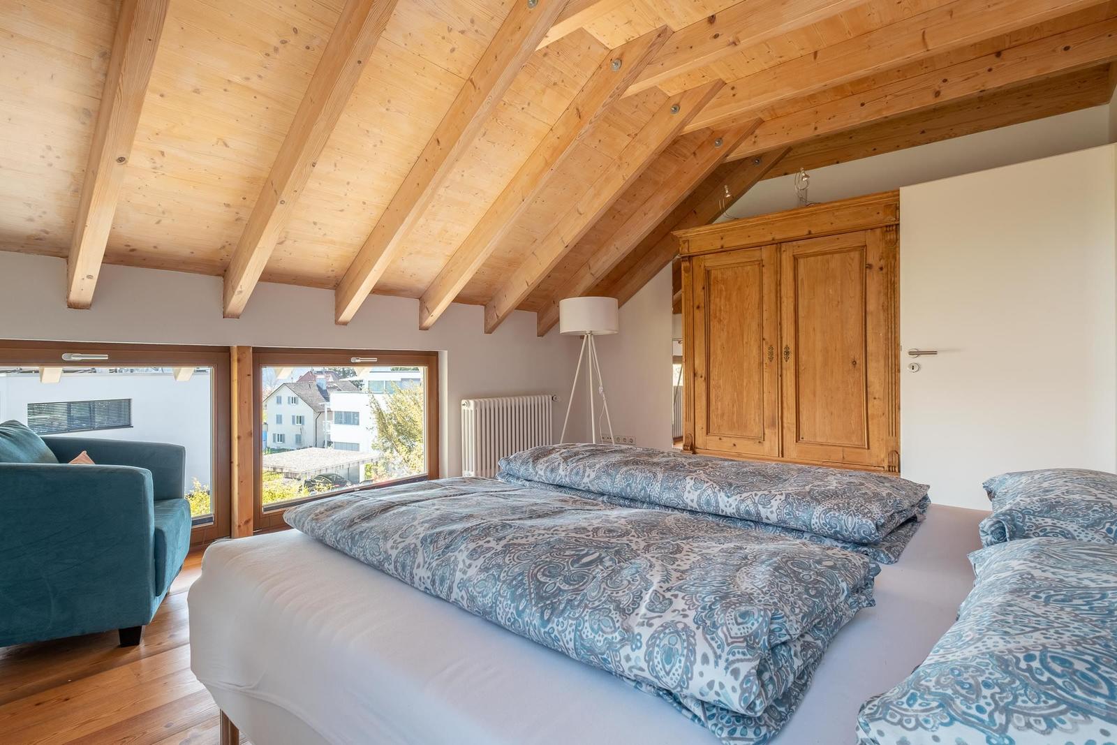 Schlafzimmer mit Holzdecke, Bett mit Muster, Kleiderschrank und Fensterblick