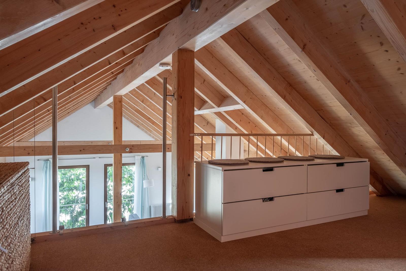 Dachgeschoss mit Holzdecke, weißen Schränken und Blick in Wohnbereich.