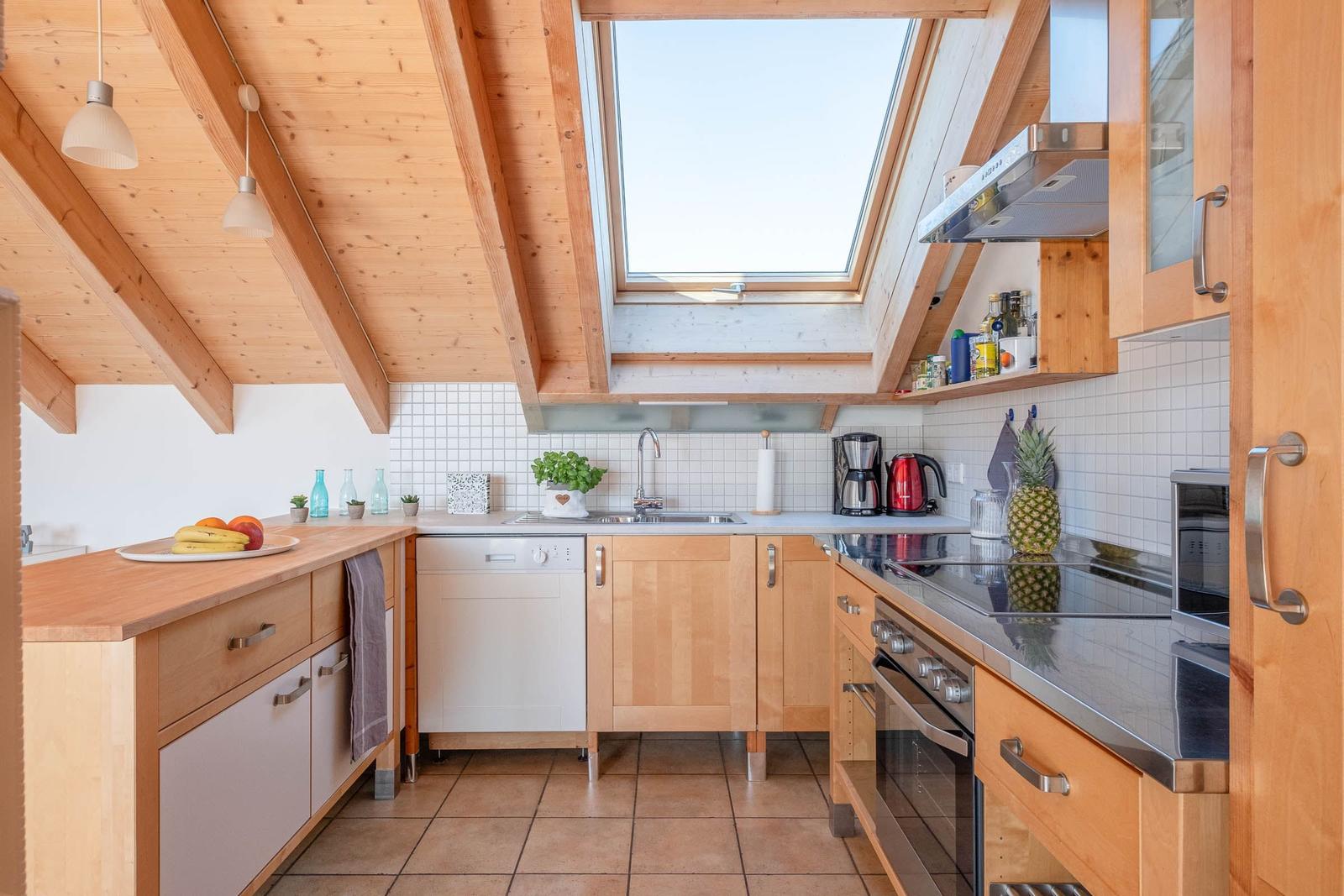 Küche mit Holzbalkendecke, Dachfenster und Edelstahlspüle.