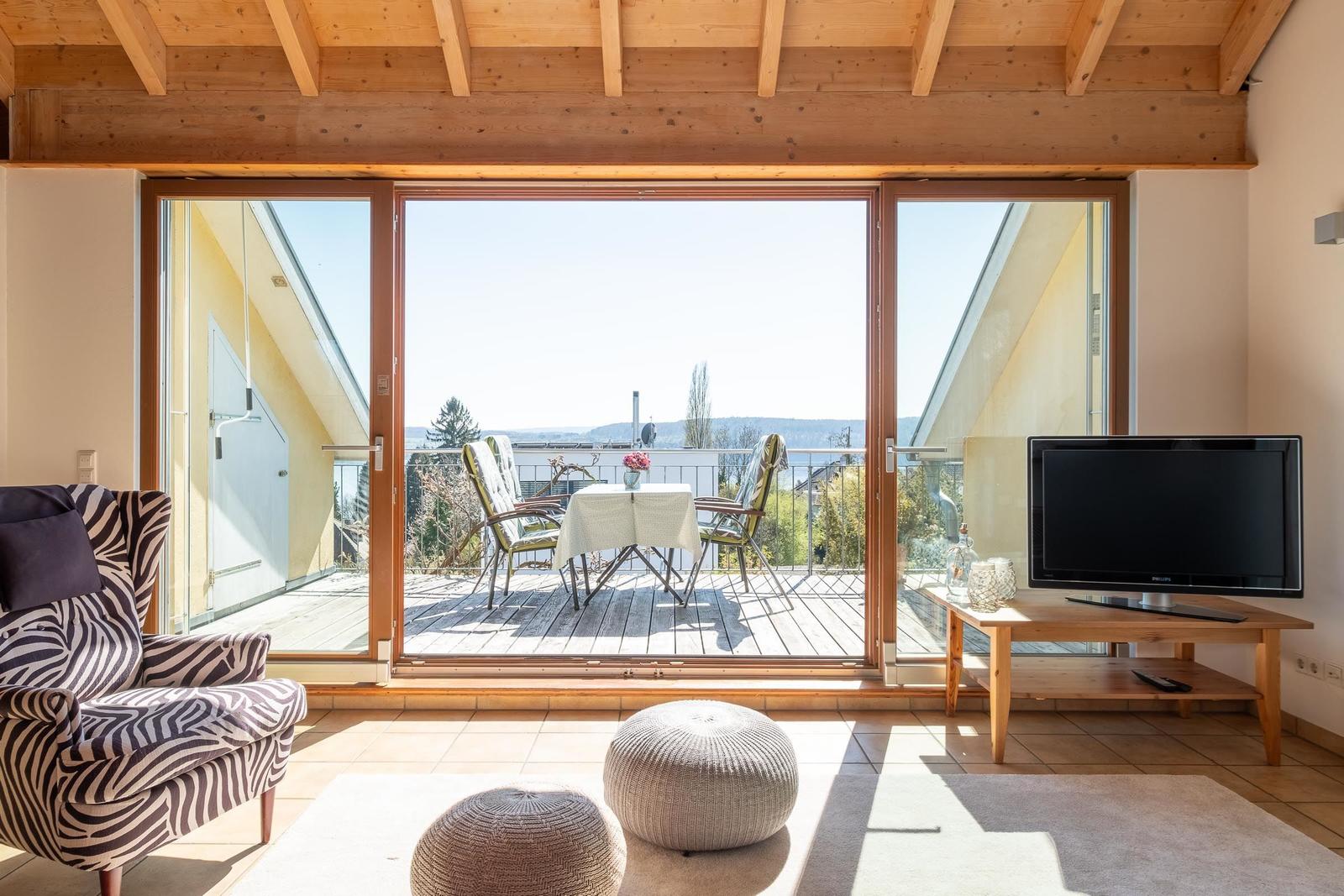 Wohnraum mit Balkon, Fernseher und Sitzgelegenheiten.