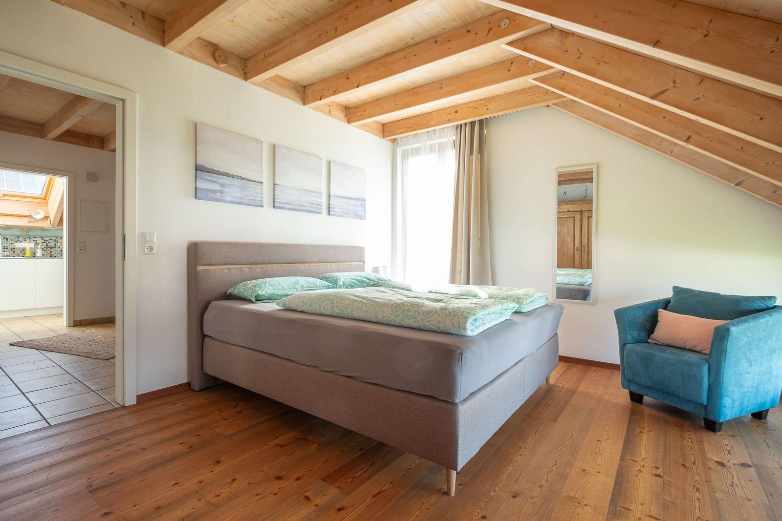 Schlafzimmer mit Bett, Sessel und Holzboden. An der Wand hängen drei Bilder.