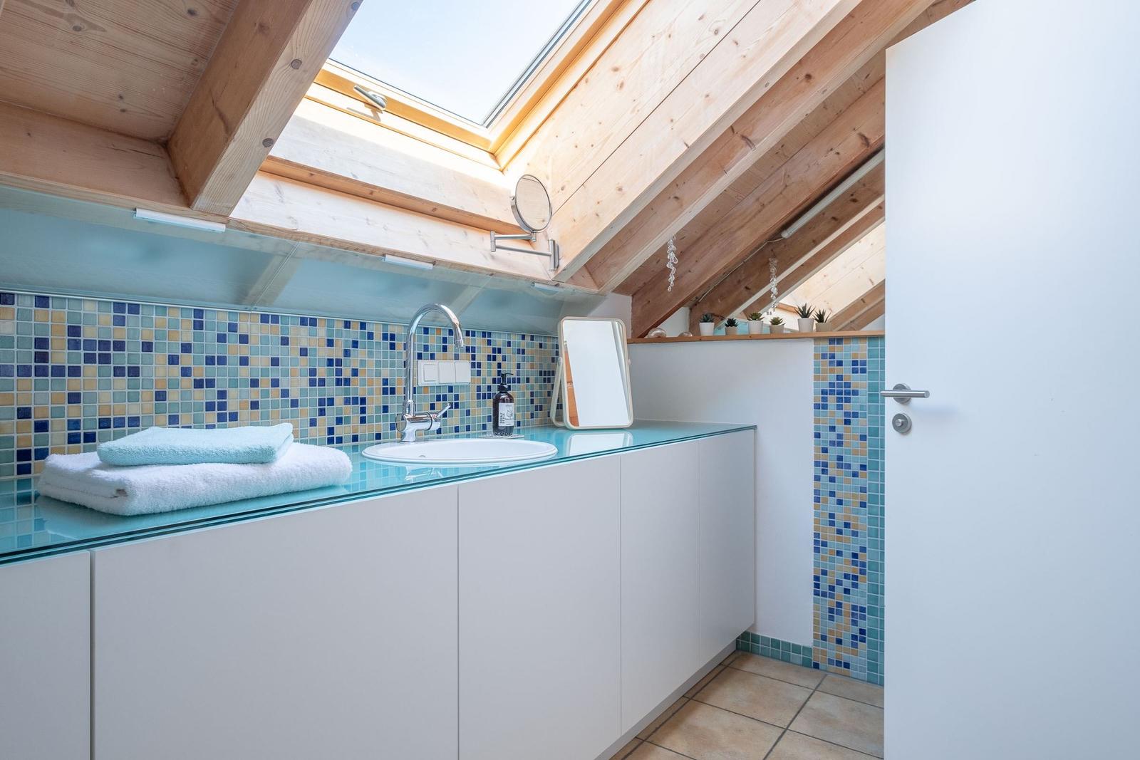 Badezimmer mit Dachschrägen, Glasarbeitsplatte und Mosaikwand