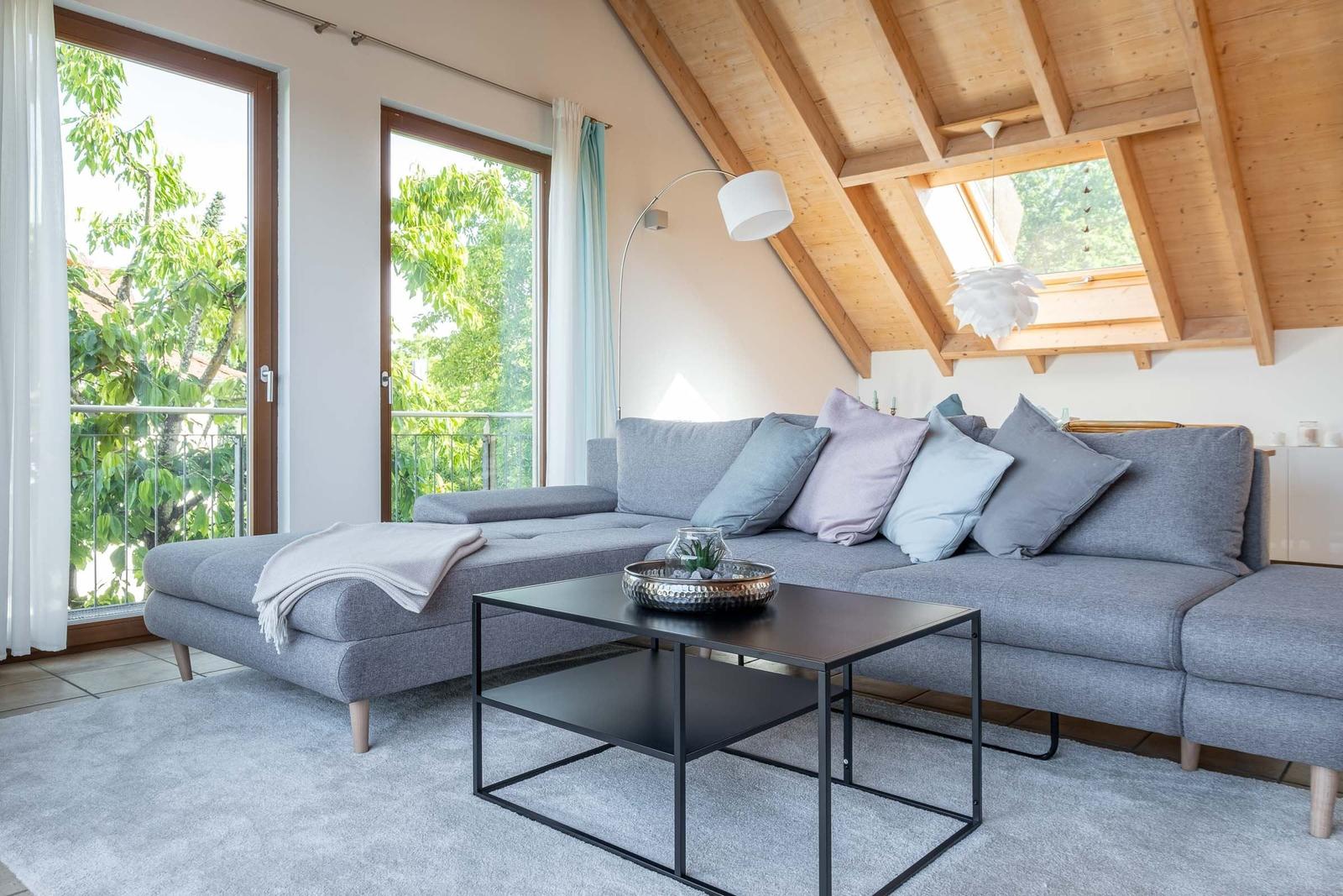 Wohnzimmer mit grauem Sofa, Tisch und Balkonblick.