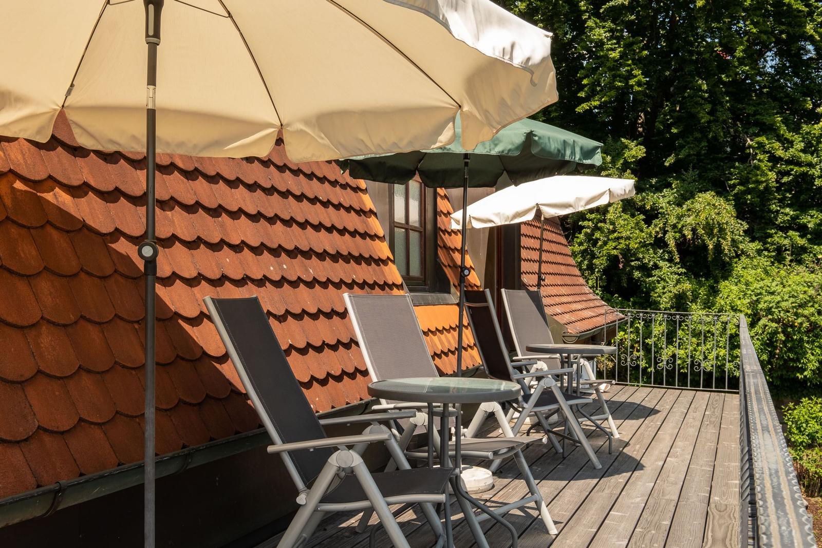 Terrasse mit Liegestühlen und Sonnenschirmen vor einem Haus mit Ziegeldach.