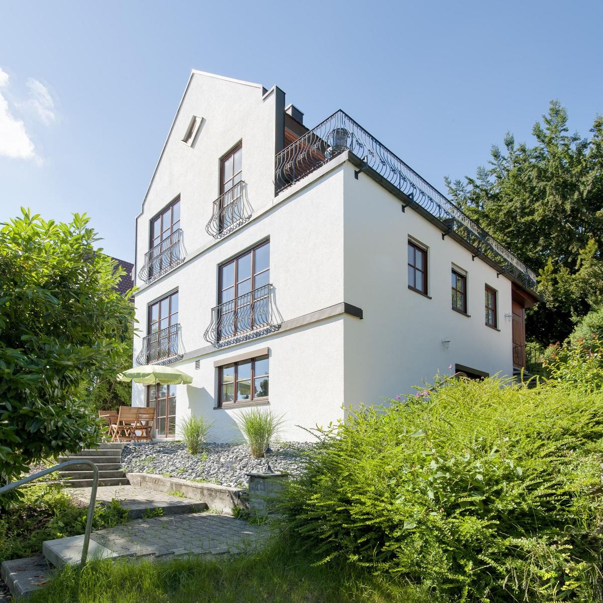 Weiße Villa mit Balkonen und Gartenbereich unter blauem Himmel.