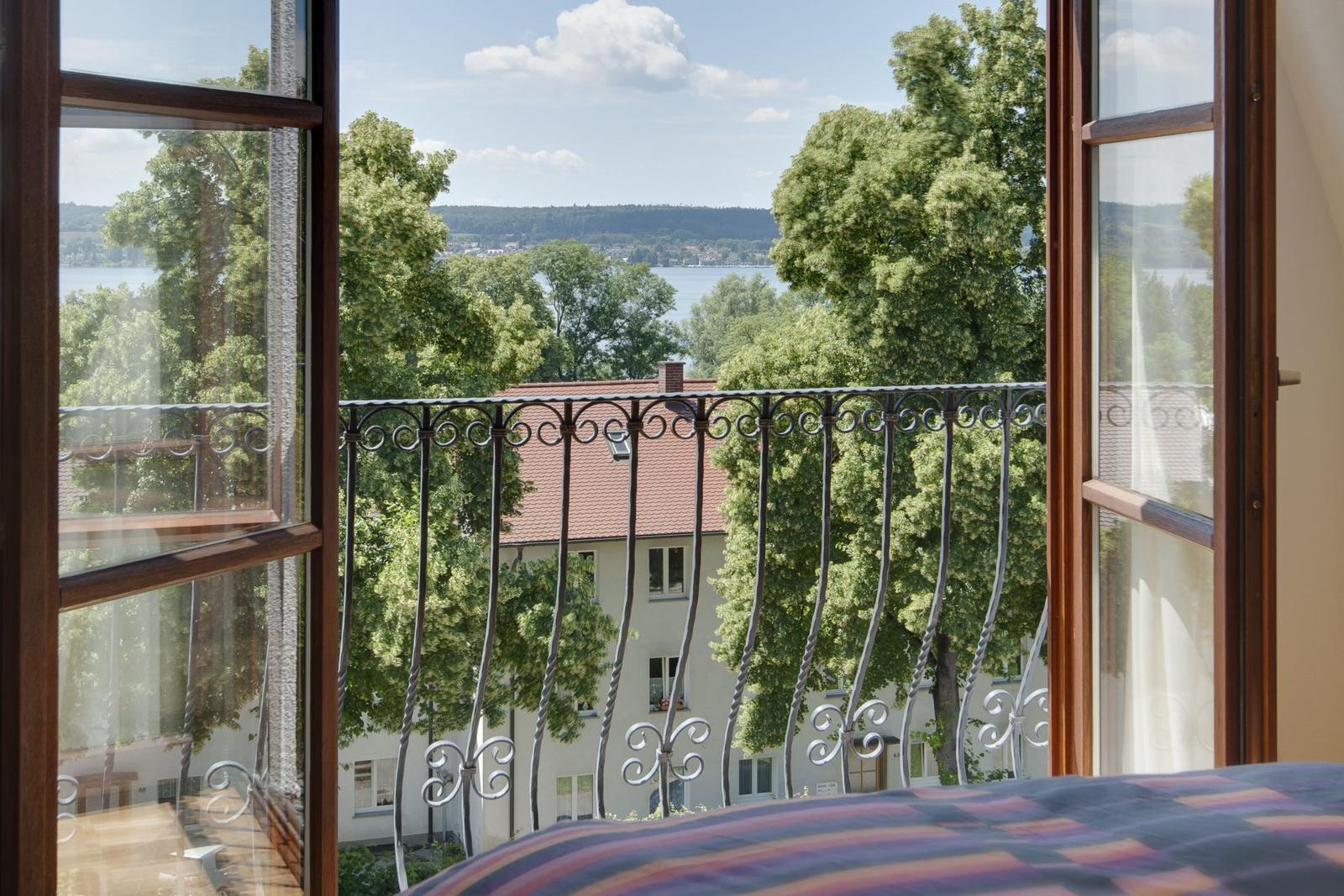 Von Balkon mit Eisengeländer Blick auf See und grüne Bäume.