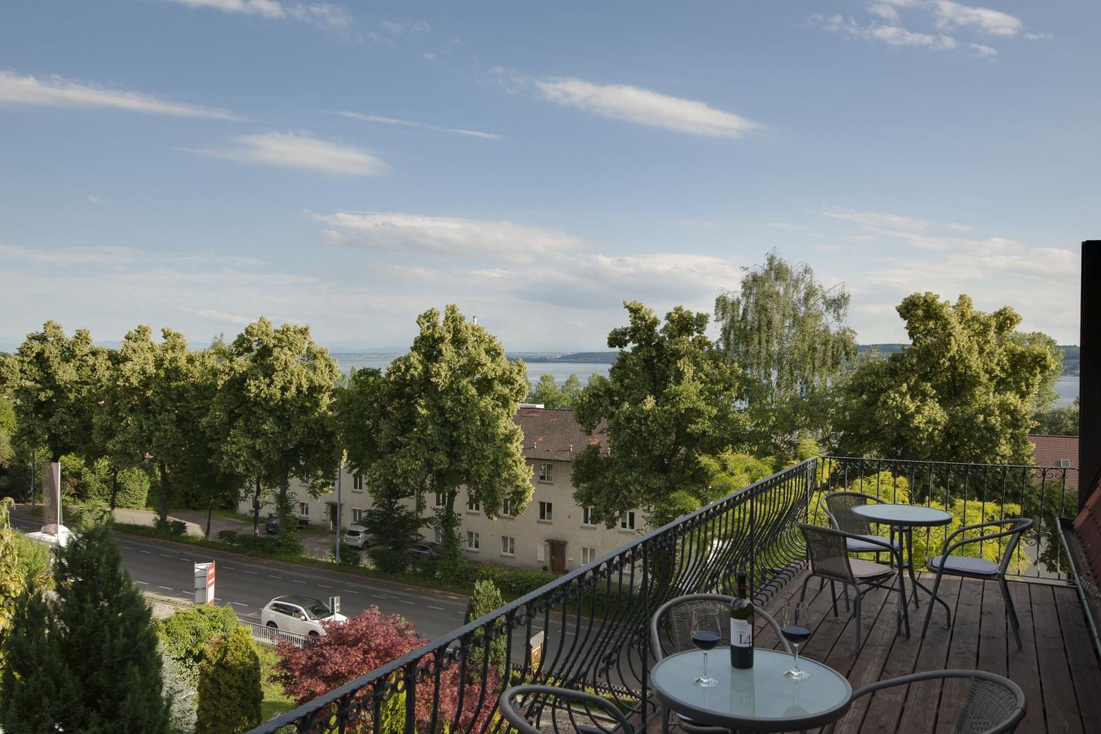 Terrasse mit Tisch und Stühlen. Blick auf Straße, Bäume und Wasser.