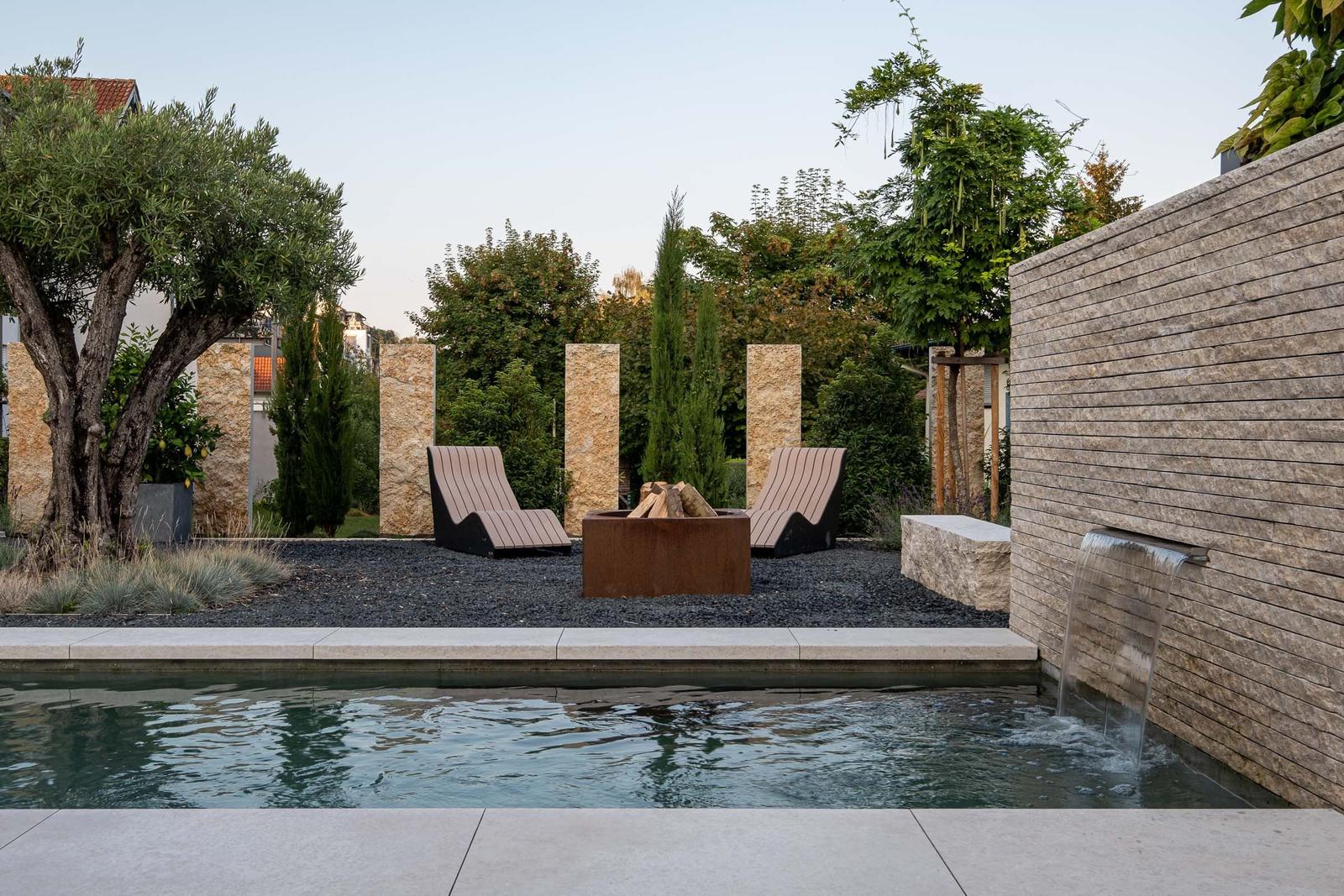 Pool mit Wasserfall, Liegen und Feuerstelle im Garten