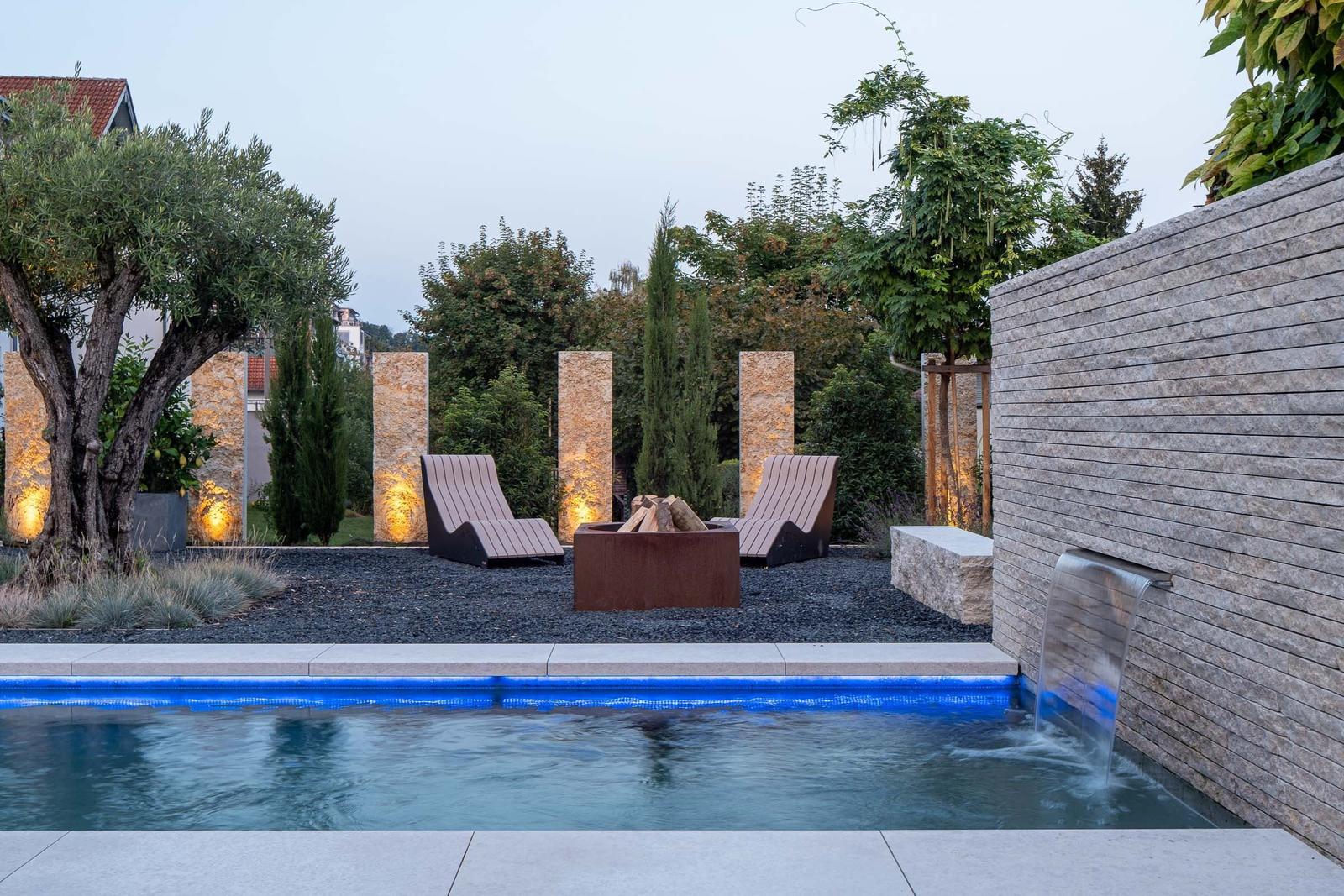 Pool mit Wasserfall, Liegestühle und Feuerkorb im Garten.