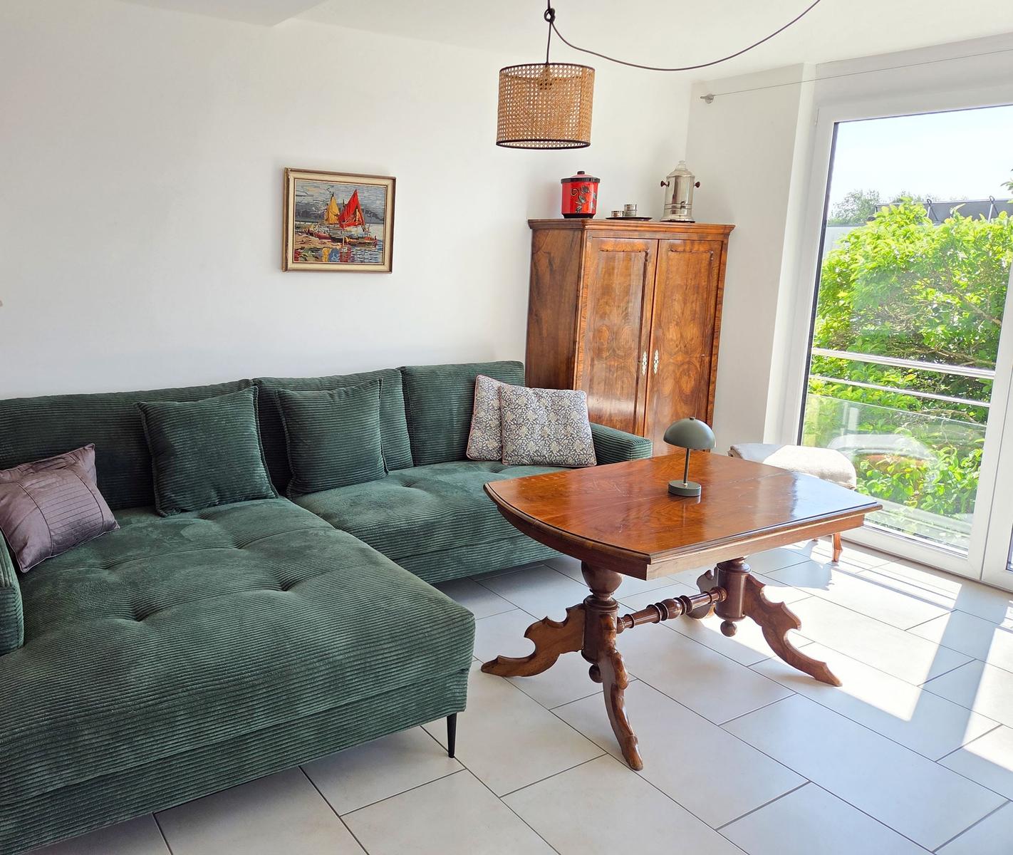 Grünes Sofa, Holztisch und Garderobe im Wohnbereich mit Blick auf Balkon.
