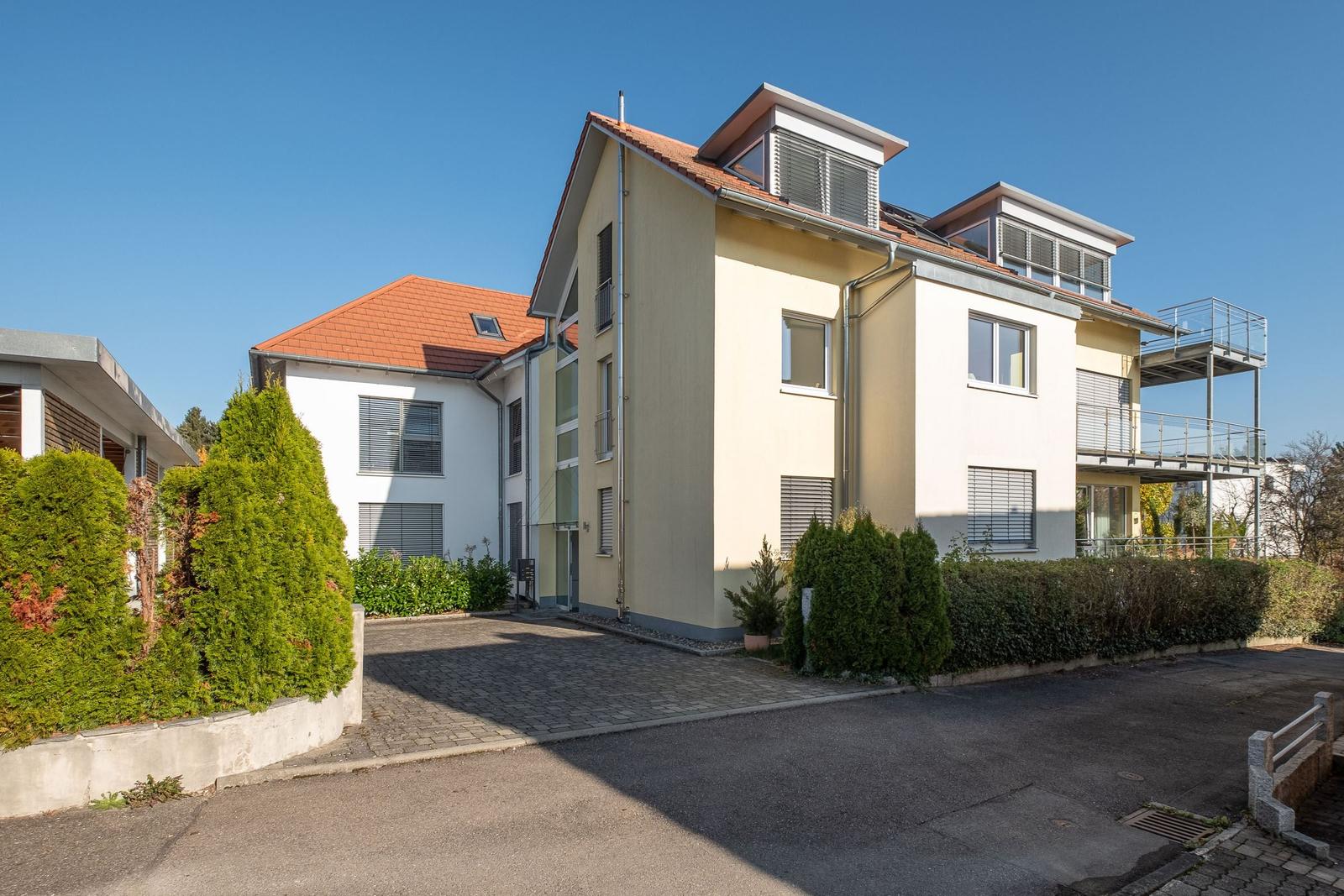 Modernes Mehrfamilienhaus mit Balkonen und begrünter Umgebung.