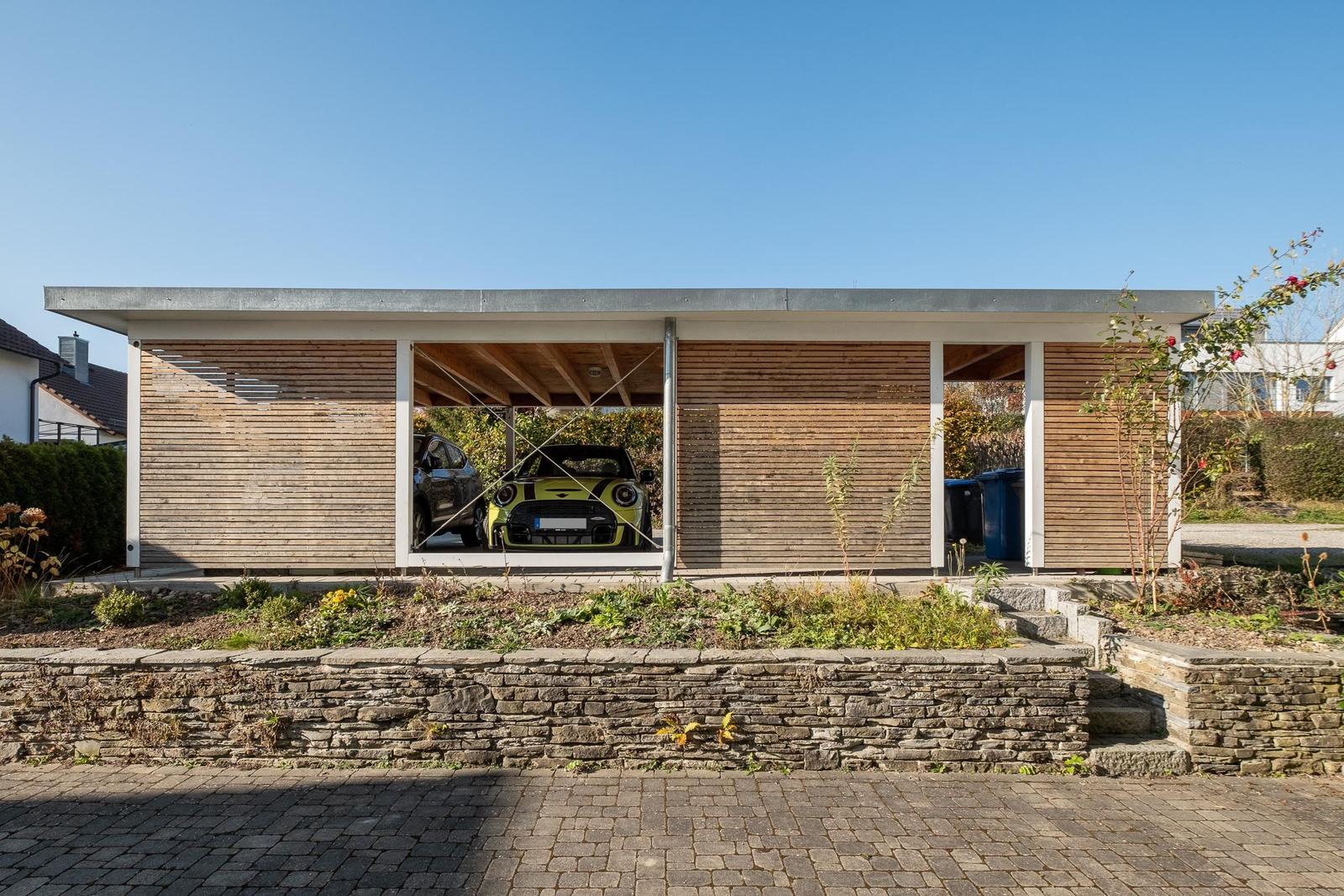 Moderne Garage mit Holzverkleidung und zwei parkenden Autos unter offenem Dach.