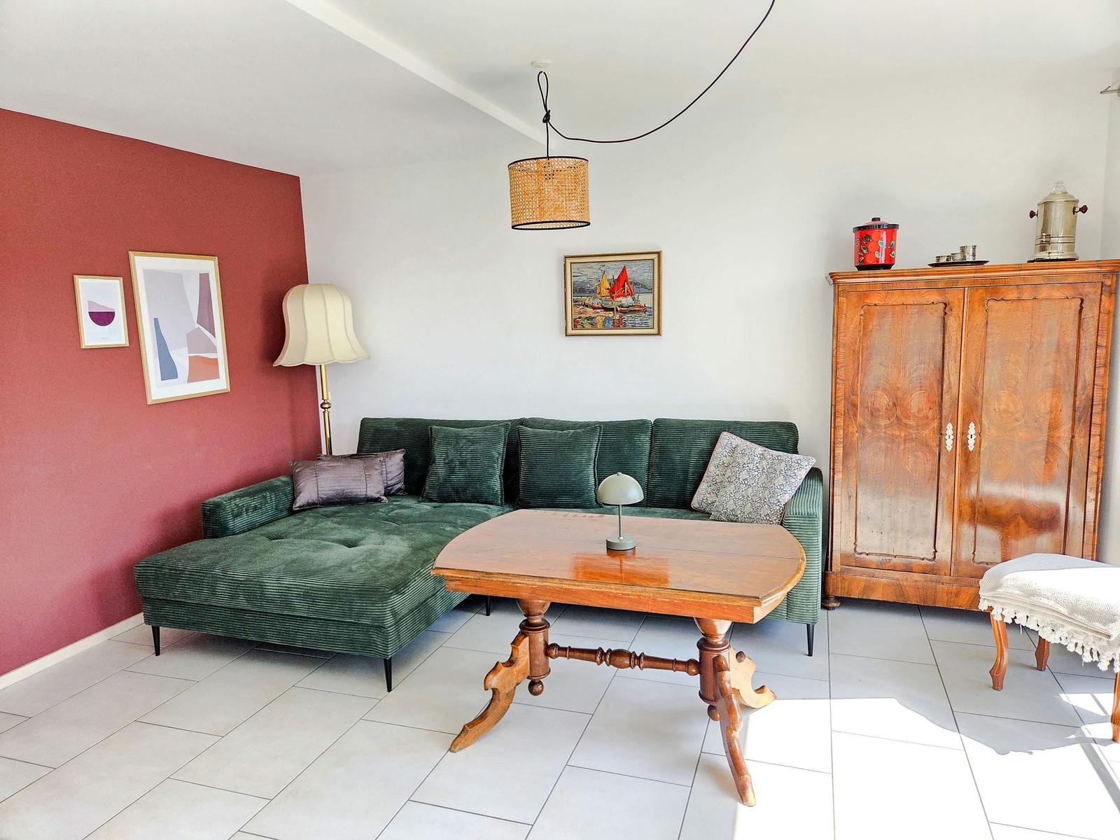 Ein Wohnzimmer mit grünem Sofa, Holztisch und antikem Schrank.