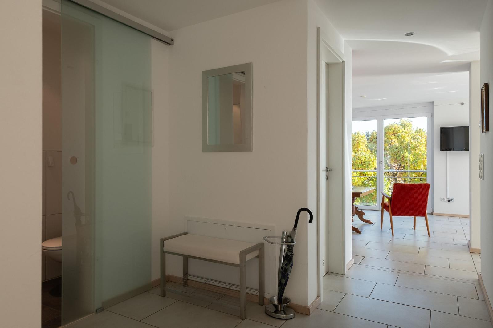 Flur mit Badezimmer und Blick auf Wohnbereich mit rotem Sessel.