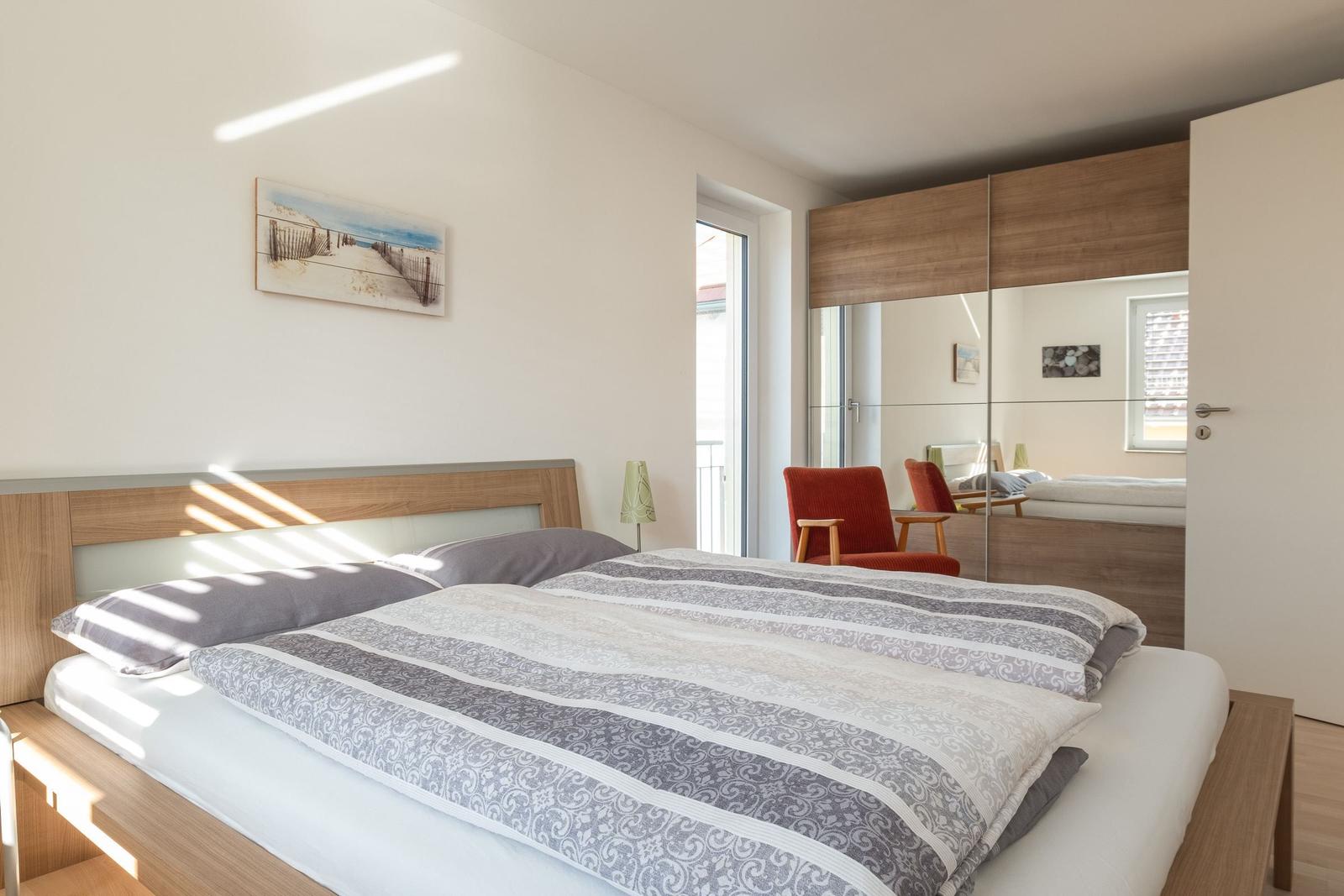 Schlafzimmer mit Doppelbett, Spiegelschrank und Fenster zum Balkon.